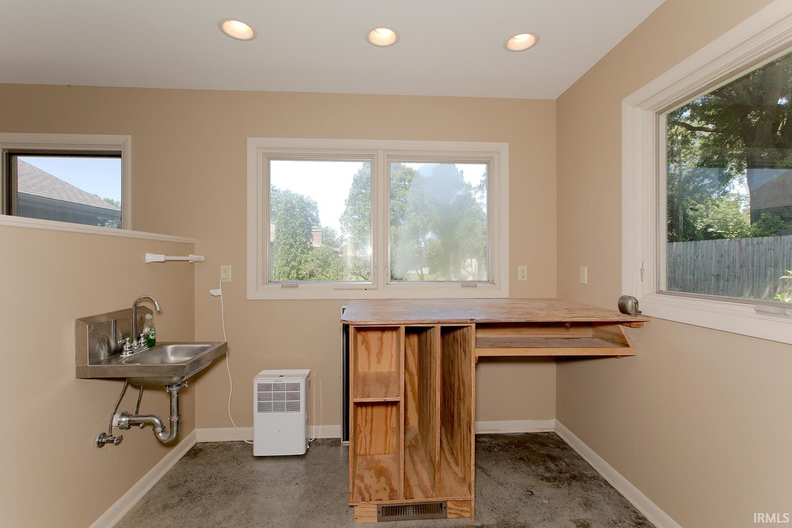 Utility room featuring a stainless steel wall-mounted sink, a built-in wood-finish workbench with storage, recessed lighting, and multiple windows
