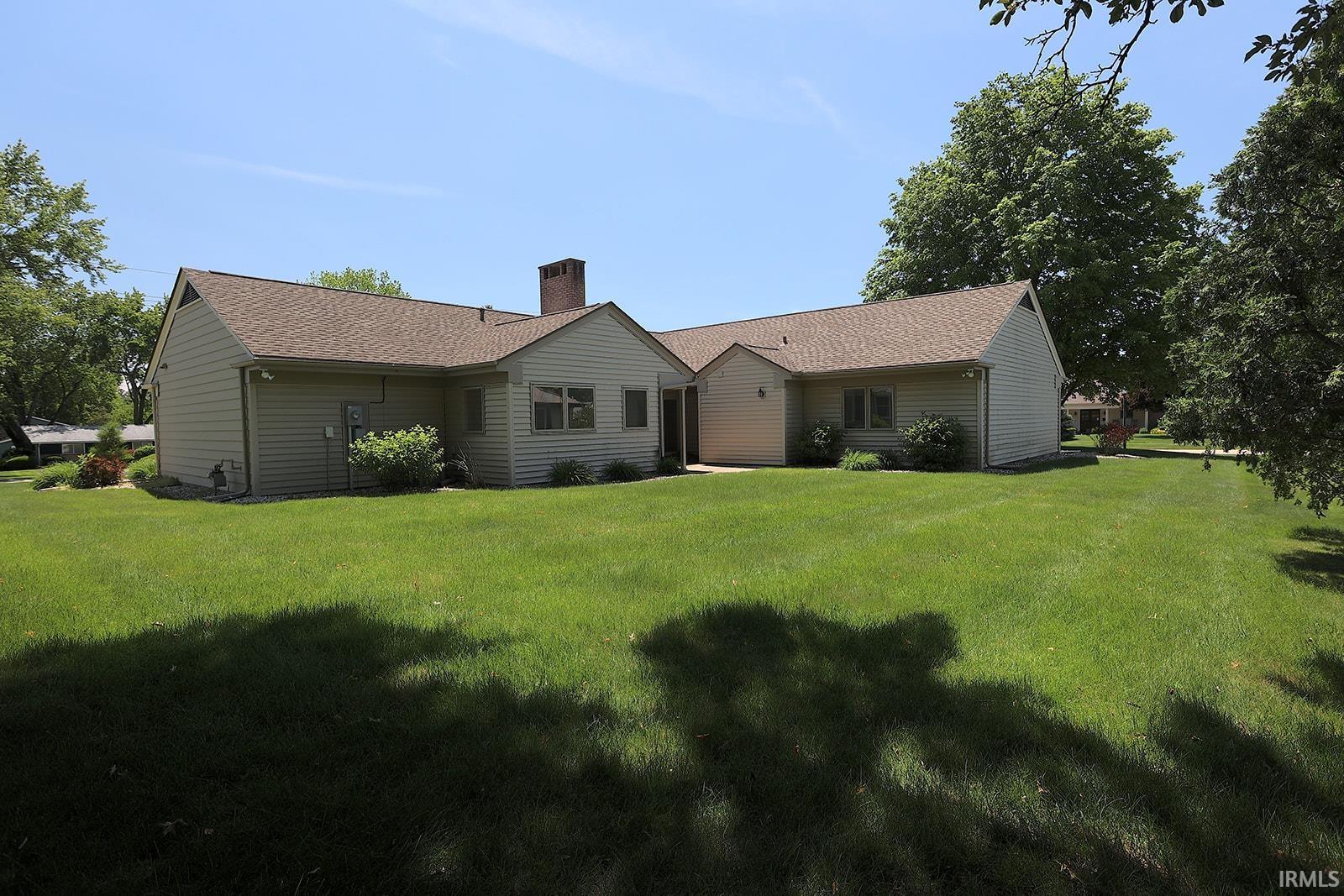 Expansive green lawn surrounds a single-story residence with light-colored siding and a brown shingle roof