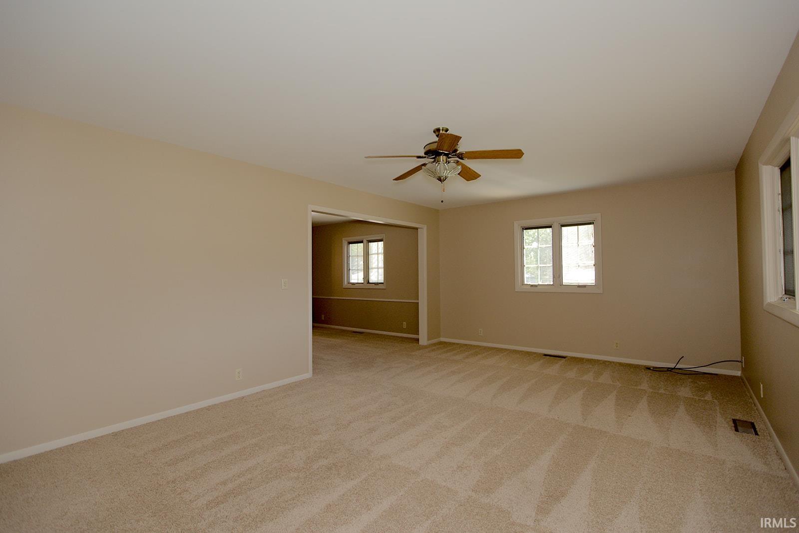 Spacious room featuring neutral carpeting, a ceiling fan with light fixture, and multiple windows with white trim