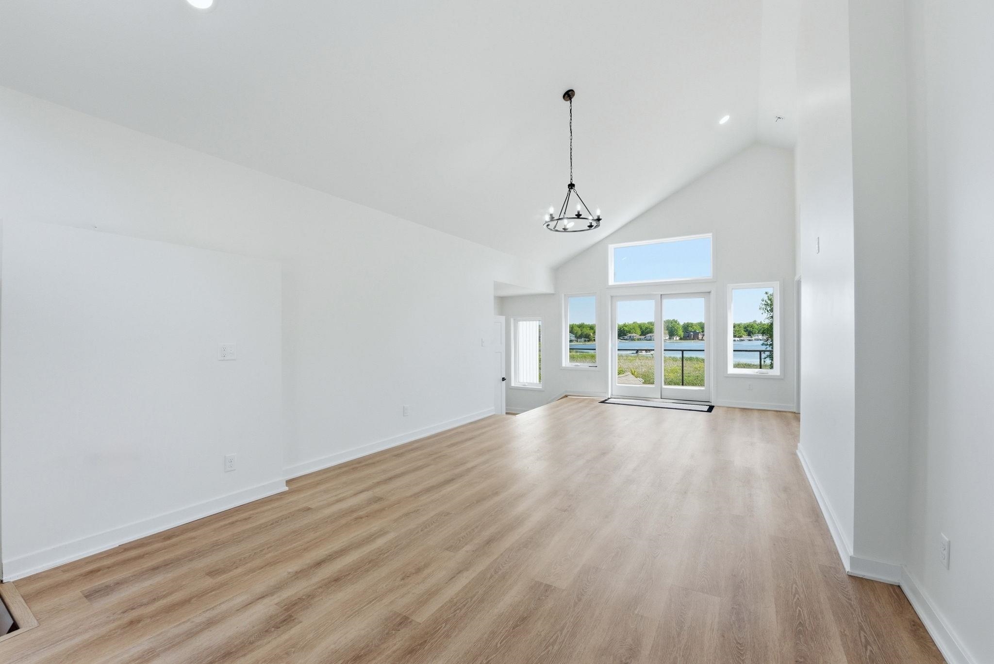 Spacious room featuring vaulted ceilings, wood-finish flooring, recessed lighting, and a contemporary chandelier