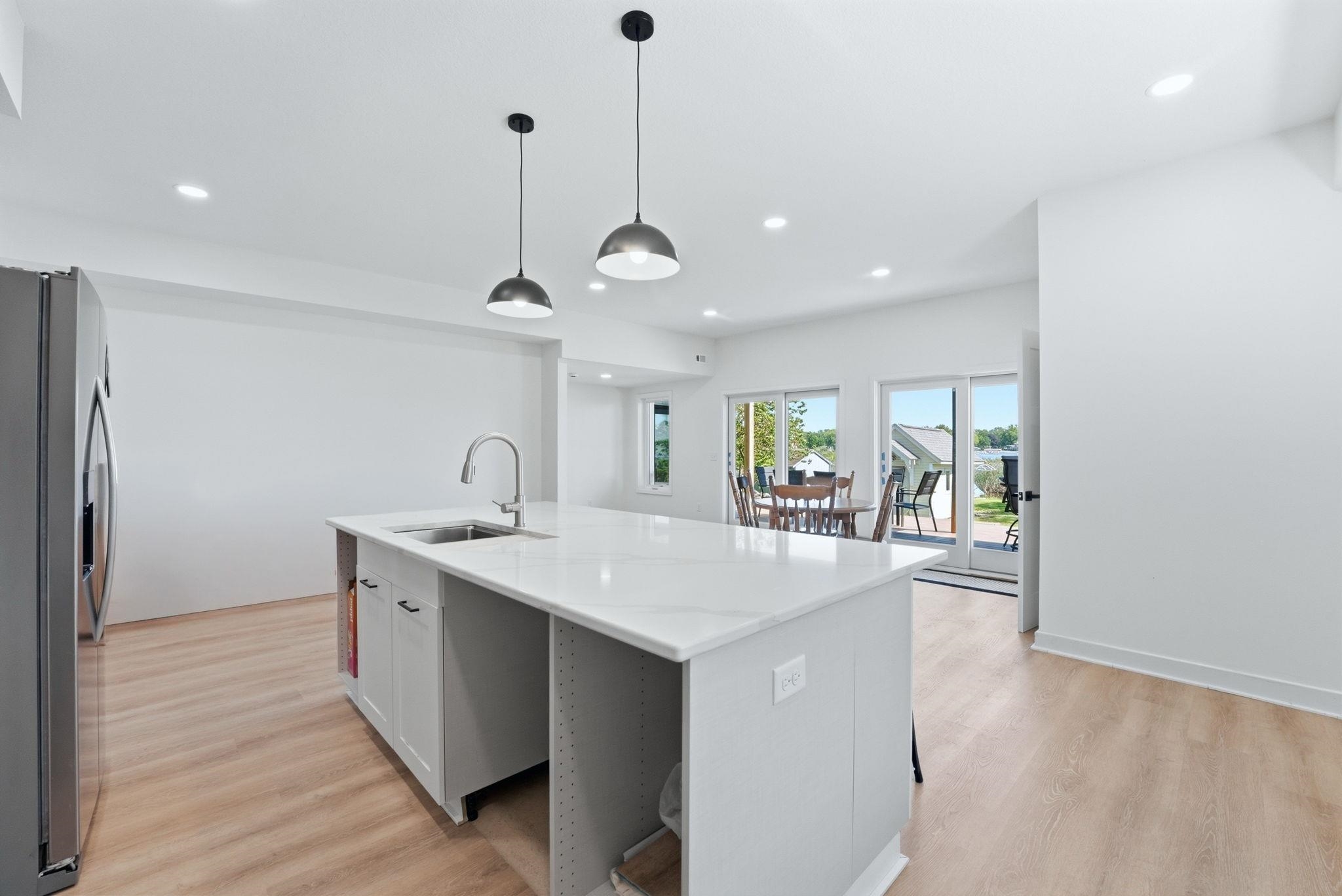 Open-concept kitchen featuring a large island with a sink, pendant lighting, recessed lighting, wood-finish flooring, and sliding glass doors leading to an exterior space
