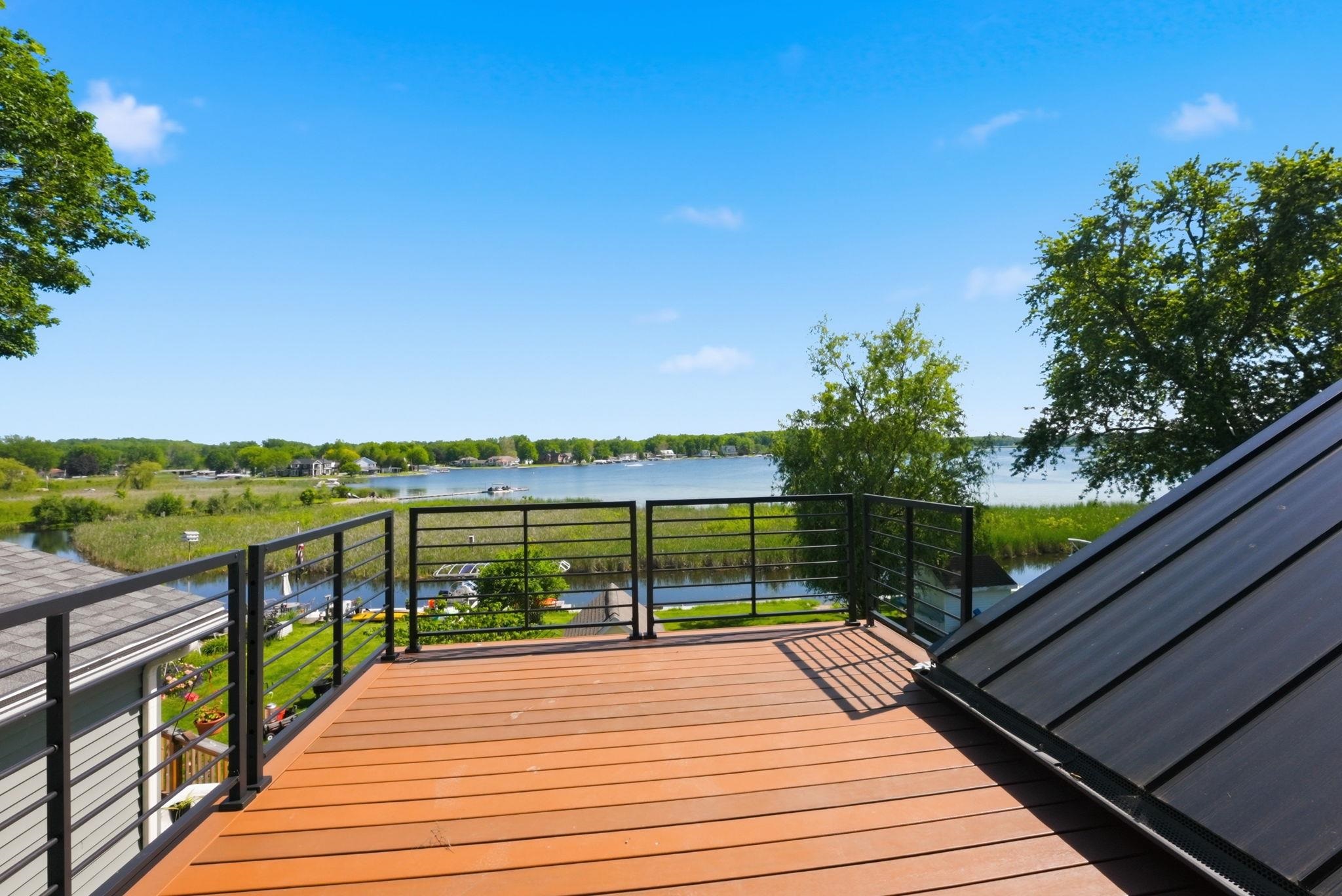 Spacious elevated deck with composite wood-finish flooring and black metal railing overlooking a tranquil body of water