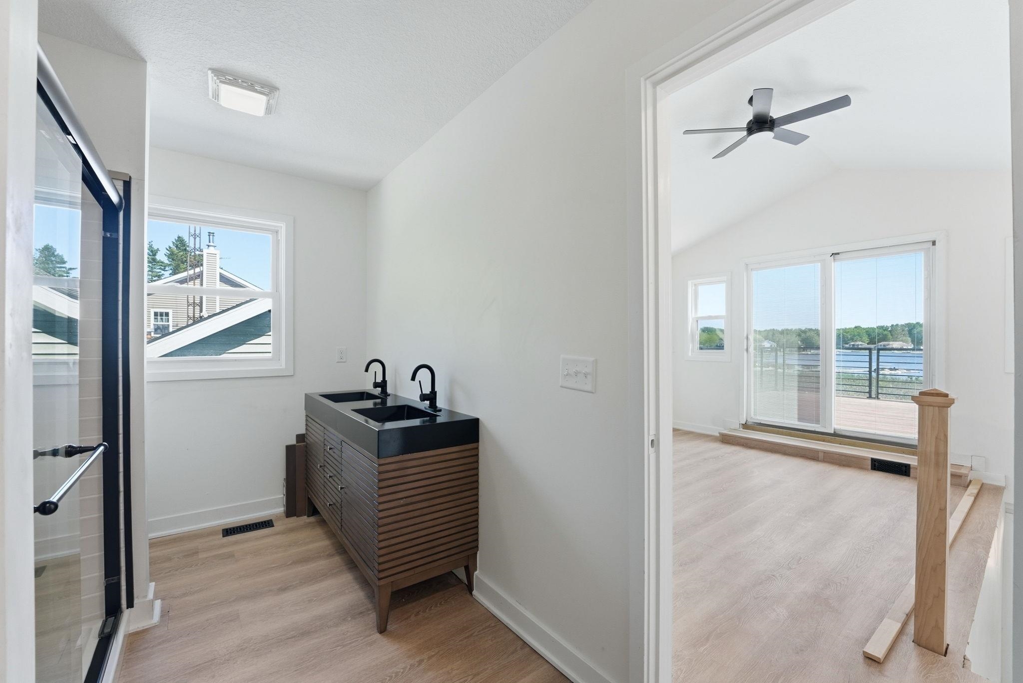 Modern bathroom featuring a double vanity with matte black fixtures, a glass-enclosed shower, and wood-finish flooring