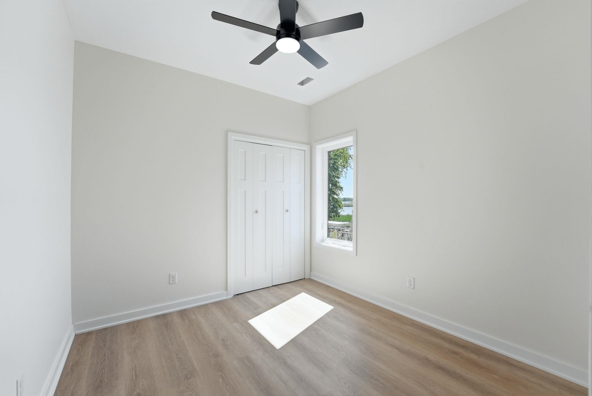 Room featuring wood-finish flooring, a contemporary ceiling fan, and a single window with a water backdrop