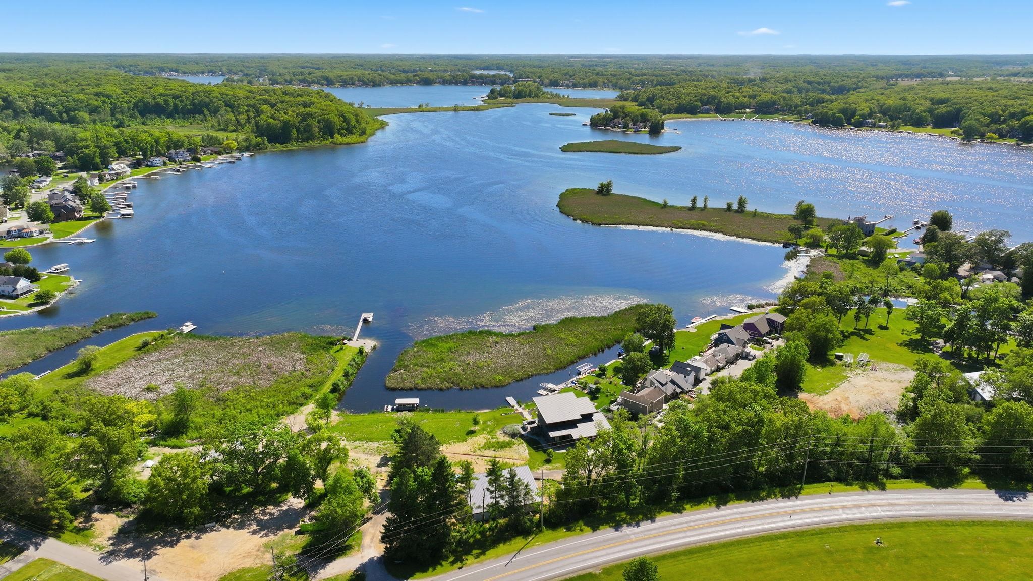 Expansive lakefront property featuring a private dock, wetland areas, a paved road, and abundant surrounding greenery