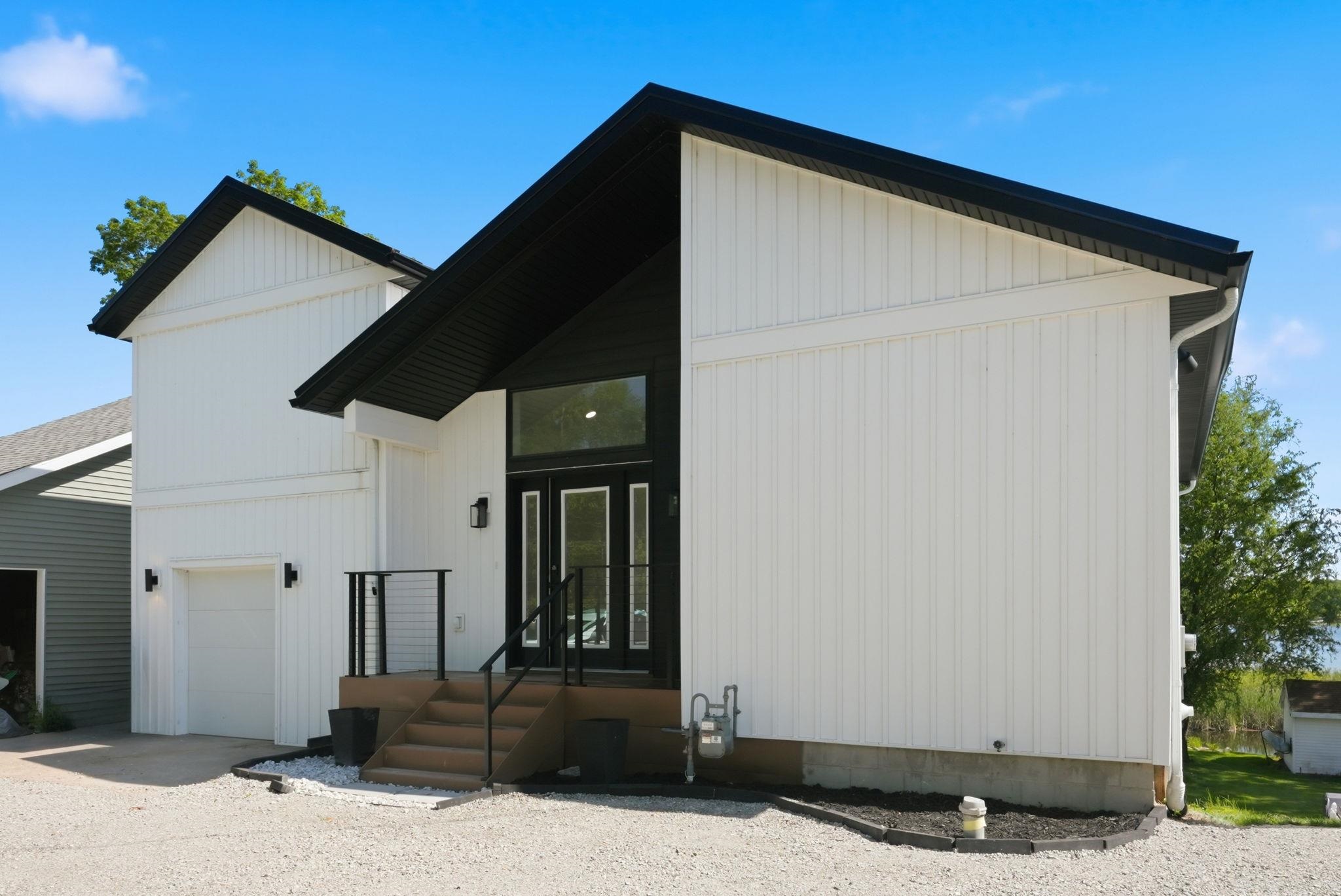Modern architectural exterior featuring white board and batten siding, black trim, and a black double entry door with transom window