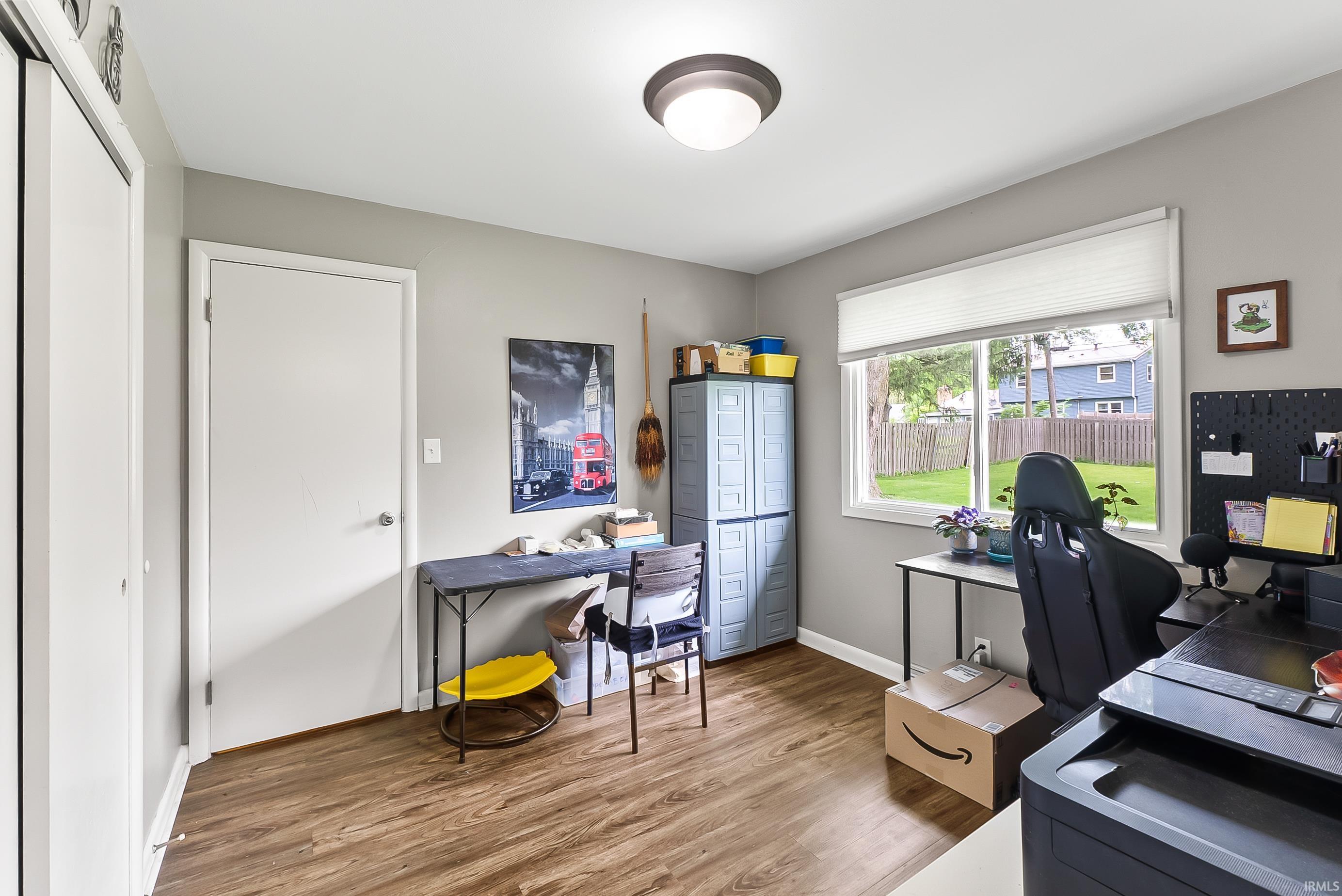 Room featuring wood-finish flooring, a window with a cellular shade, and a flush-mount ceiling light