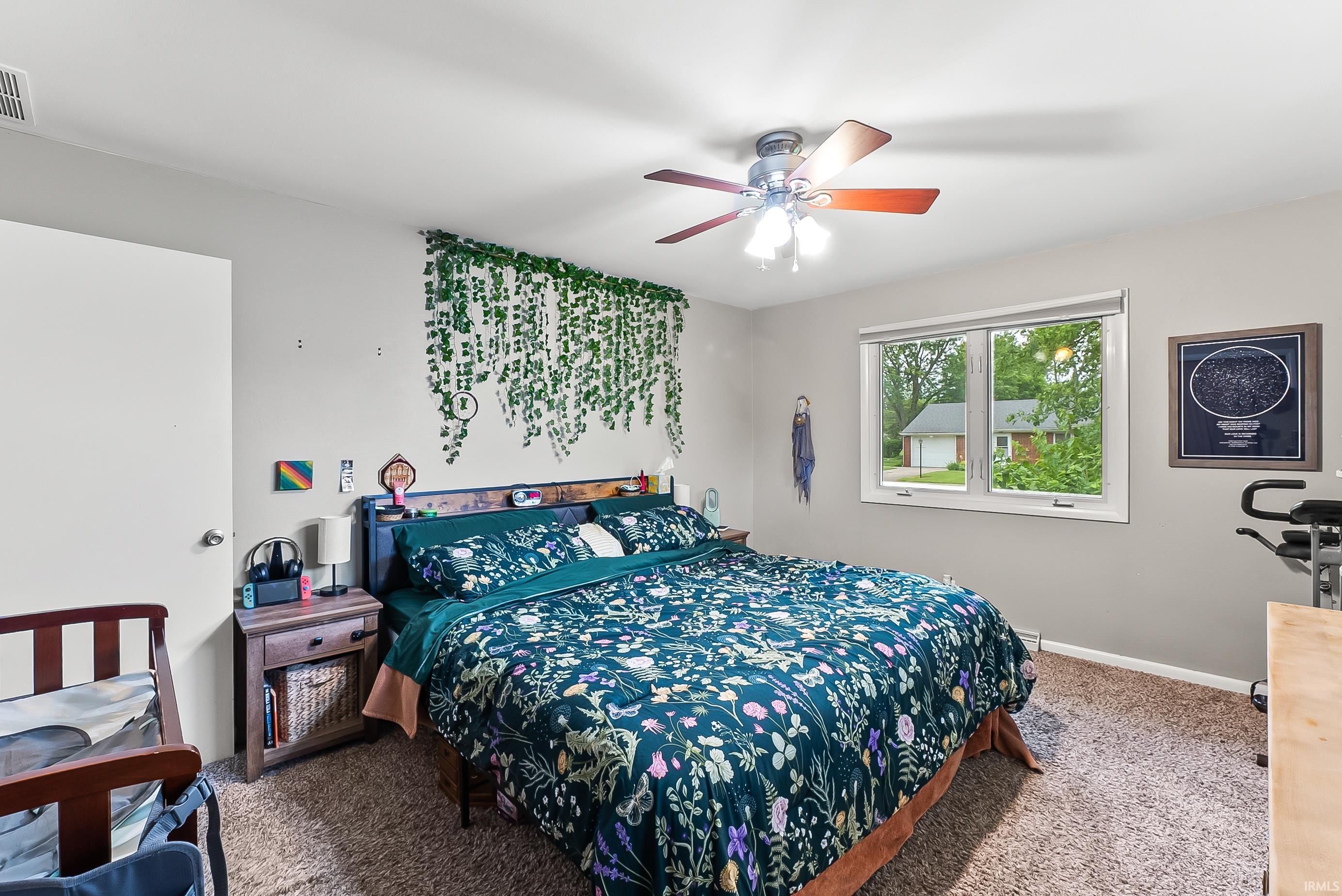 Carpeted bedroom featuring a large window, a ceiling fan with integrated lighting, and a white interior door