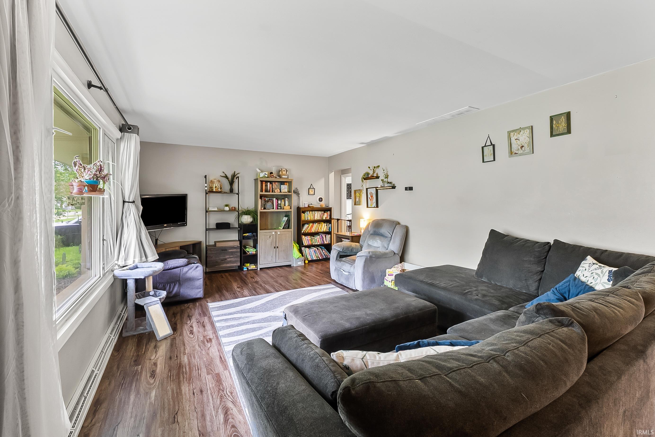 Spacious living area featuring wood-finish flooring, light grey wall tones, and ample natural light from multiple windows