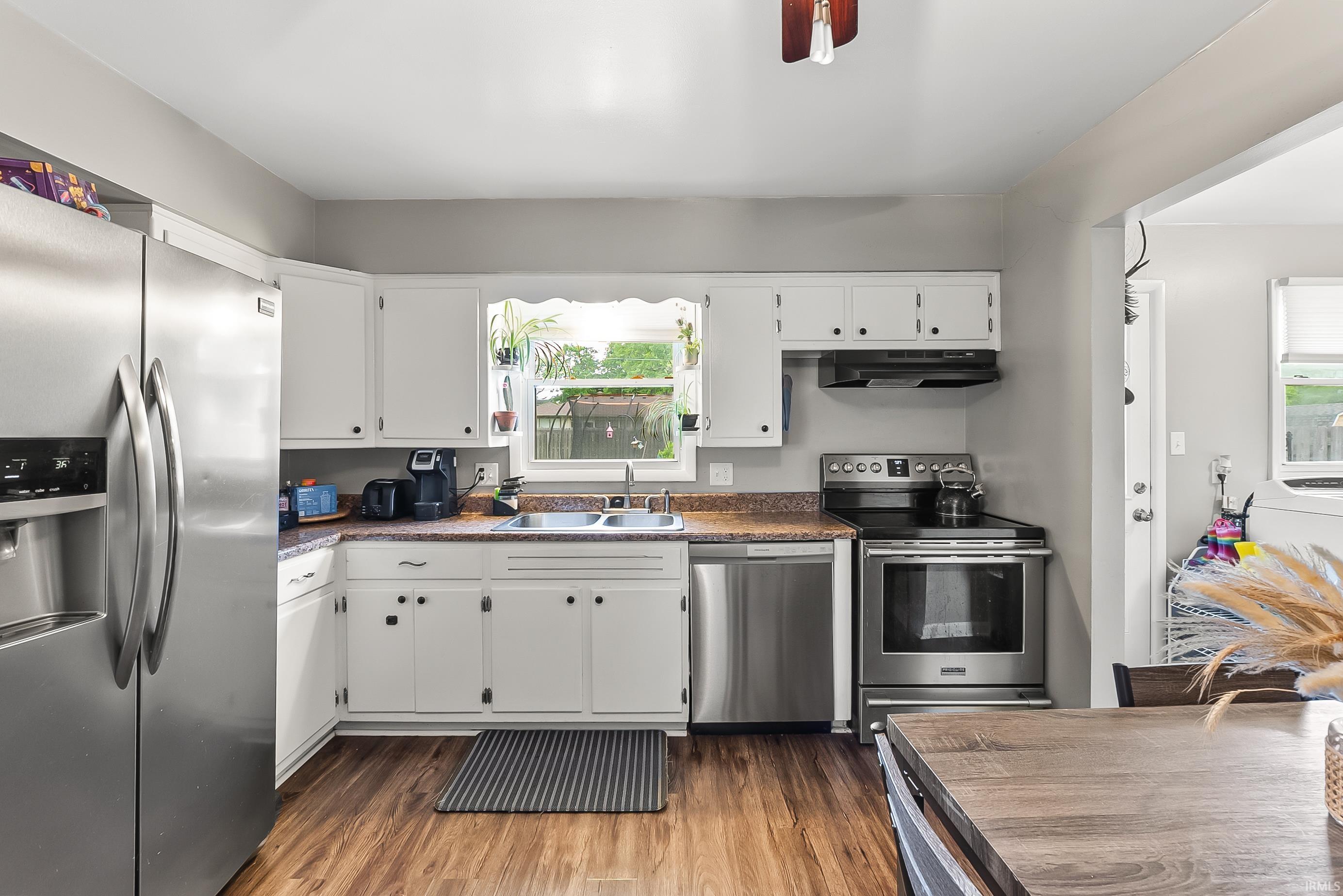 Kitchen featuring white cabinetry, wood-finish flooring, and stainless steel appliances including a refrigerator, dishwasher, and range