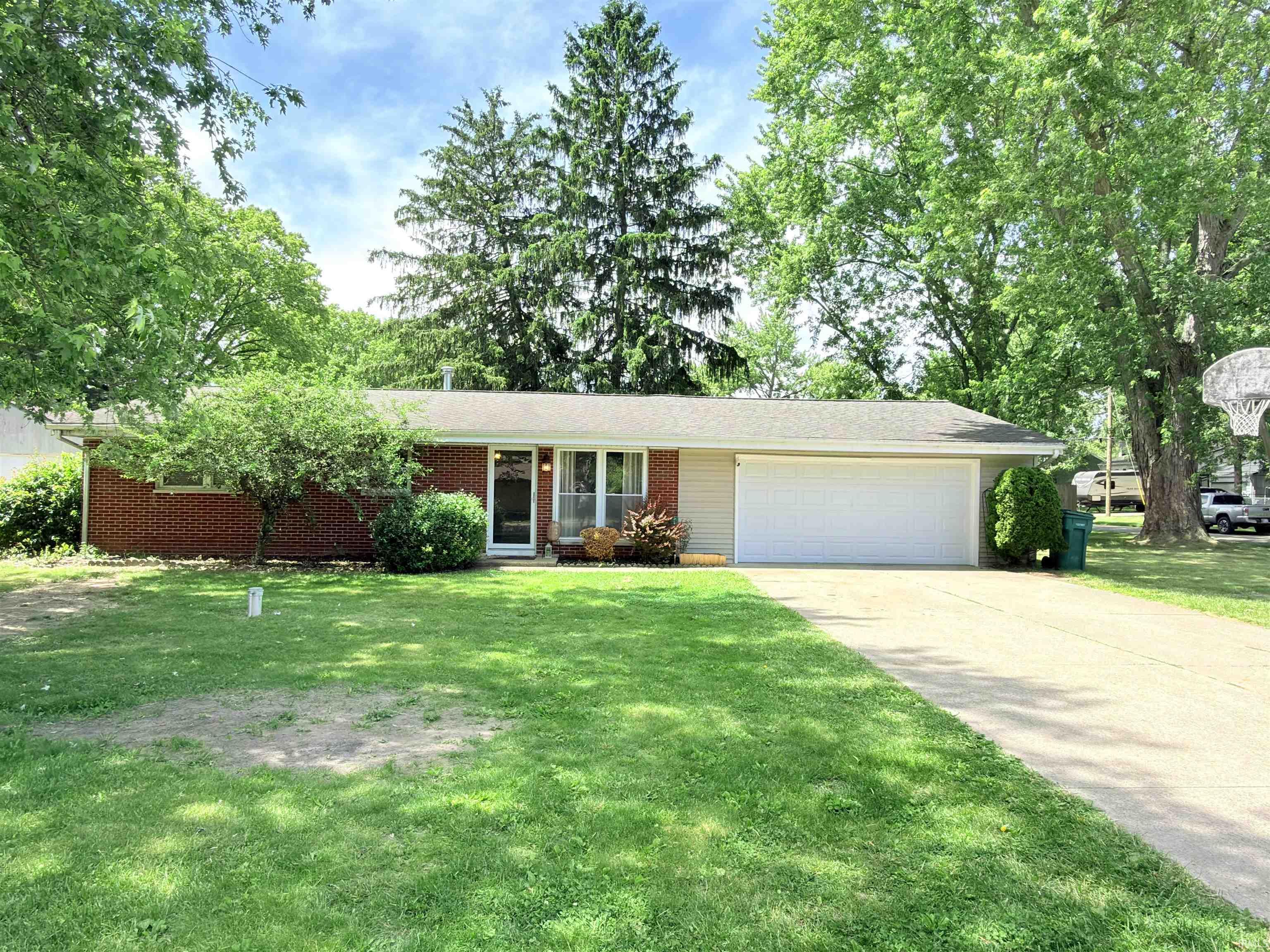 Ranch-style exterior featuring brick and siding, a two-car garage, and mature trees