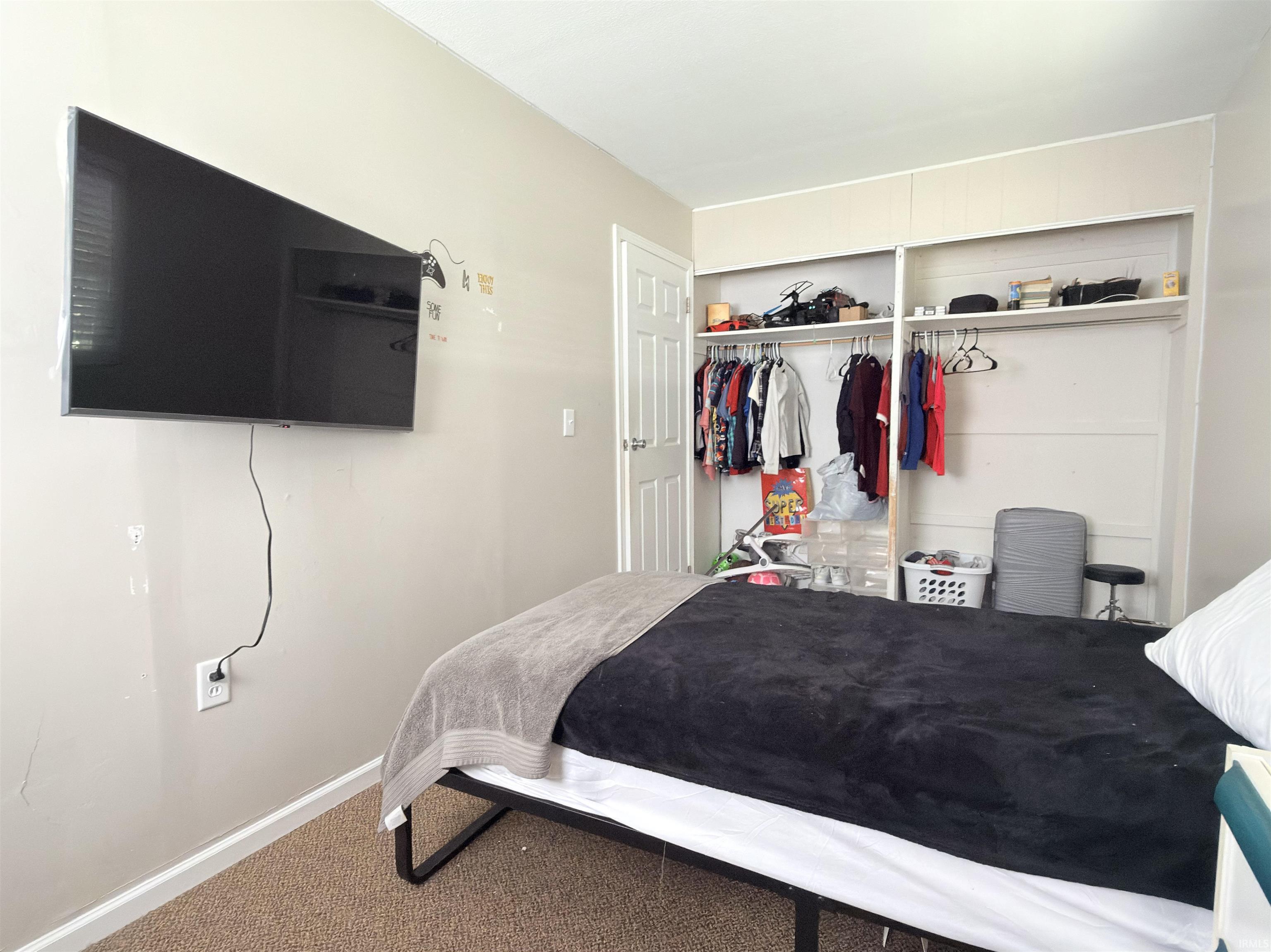 Carpeted bedroom featuring built-in open shelving and clothing rods, a white paneled door, and a wall-mounted television bracket
