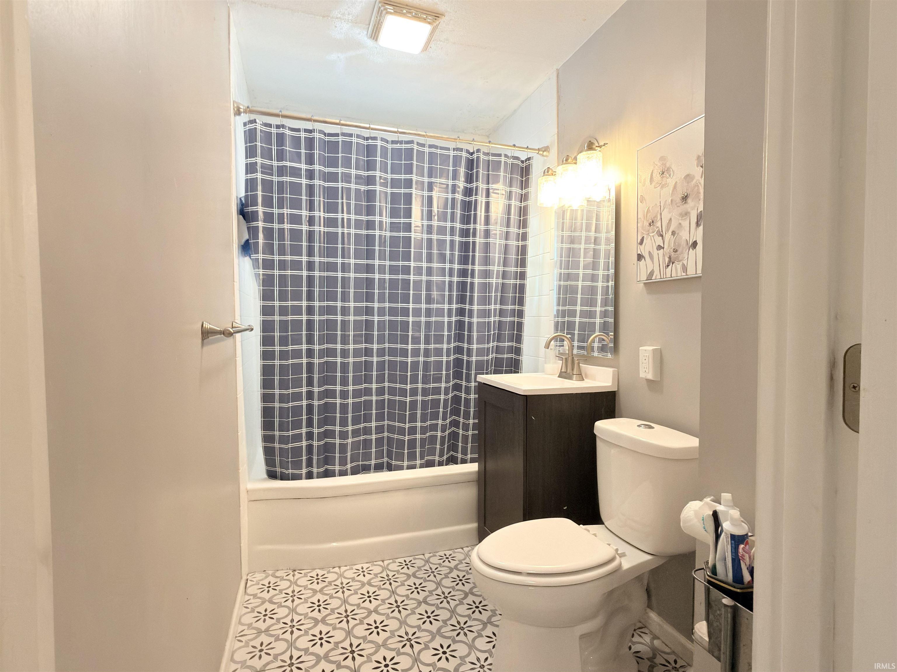 Bathroom featuring patterned floor tiles, a white bathtub with a shower, a dark wood vanity with a white countertop and sink, and a toilet