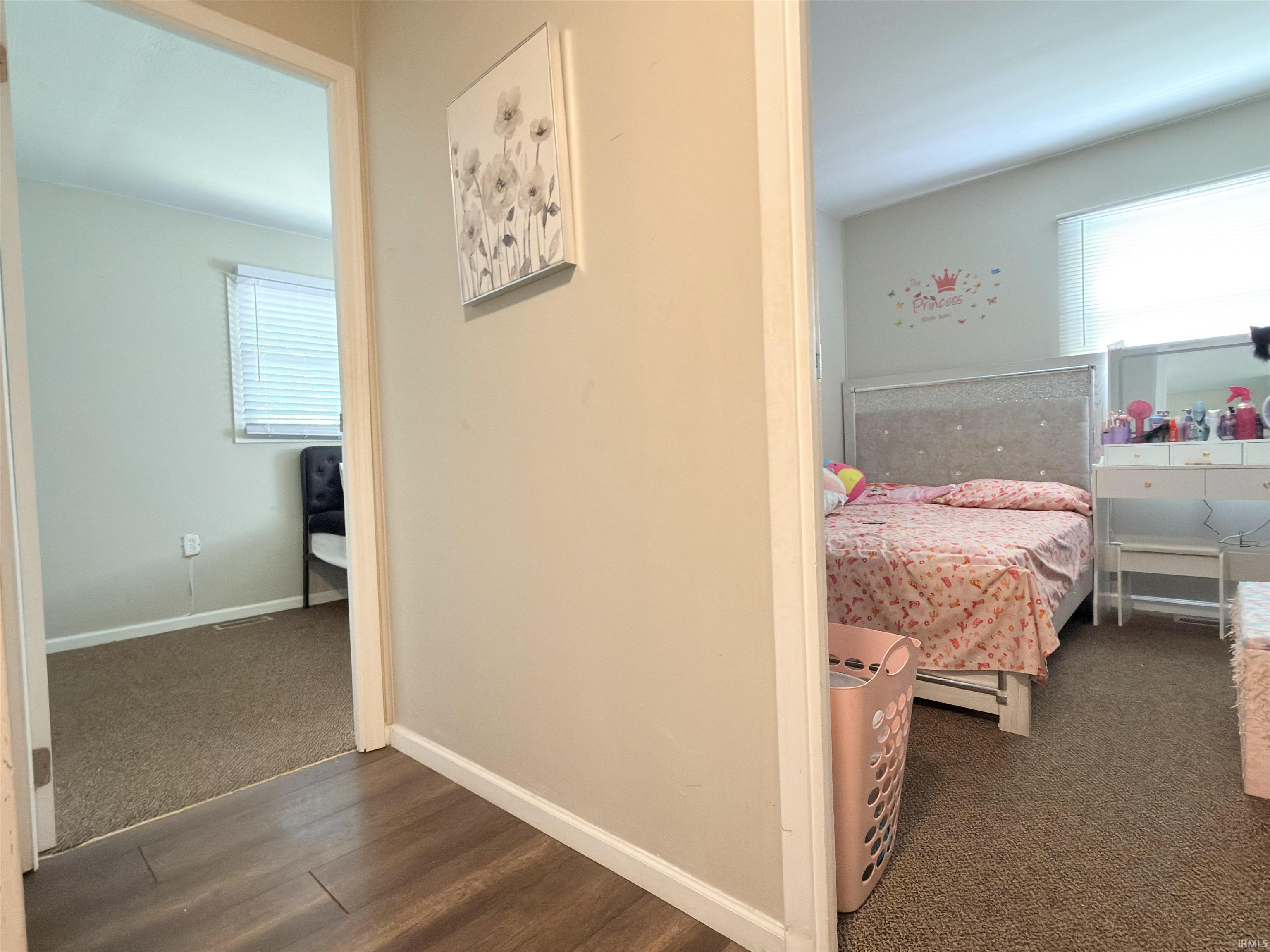 Hallway featuring wood-finish flooring, leading to two separate rooms with carpeted floors