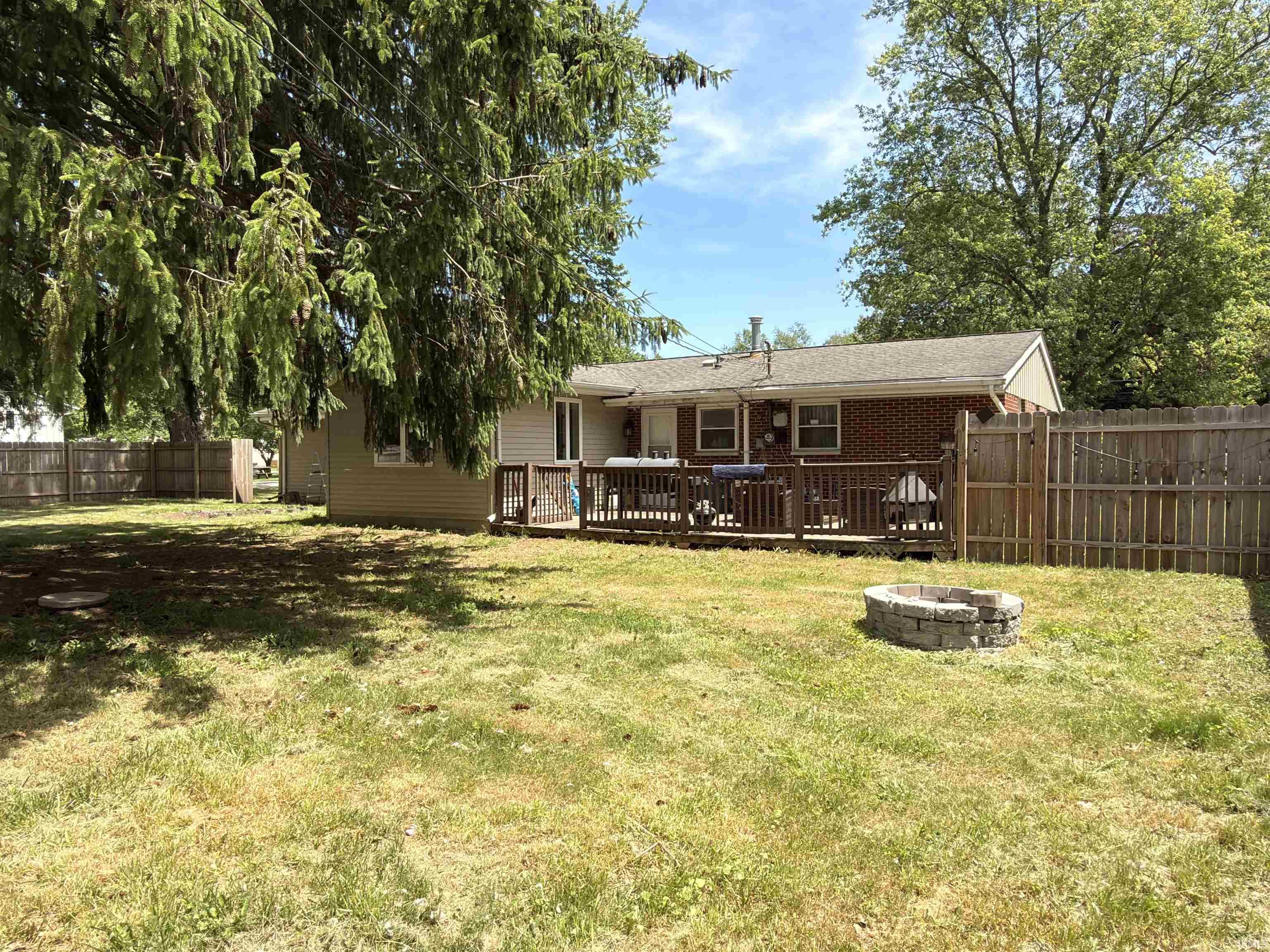 Expansive backyard featuring a wood deck, brick-clad home exterior, wood fencing, and a stone fire pit