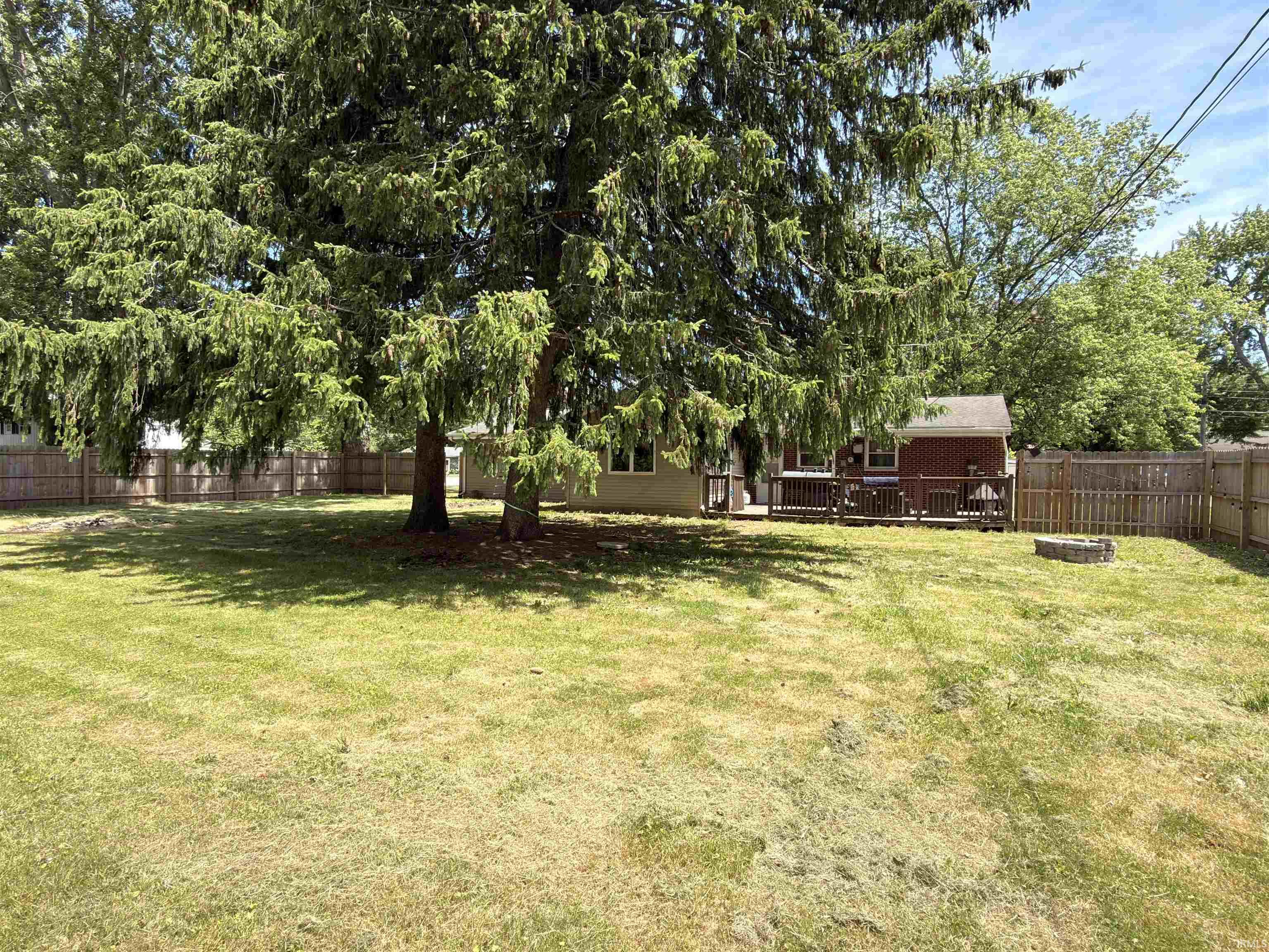 Spacious backyard featuring a large tree providing ample shade, a wood privacy fence, and a stone fire pit
