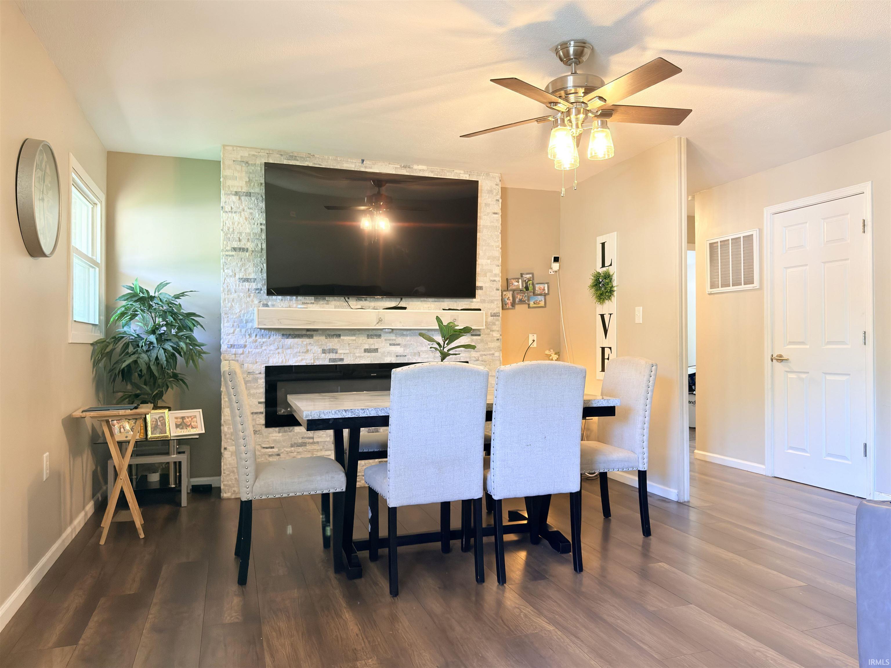Living area featuring a textured tile fireplace surround with a mantel, a ceiling fan with integrated lighting, wood-finish flooring, and neutral wall tones