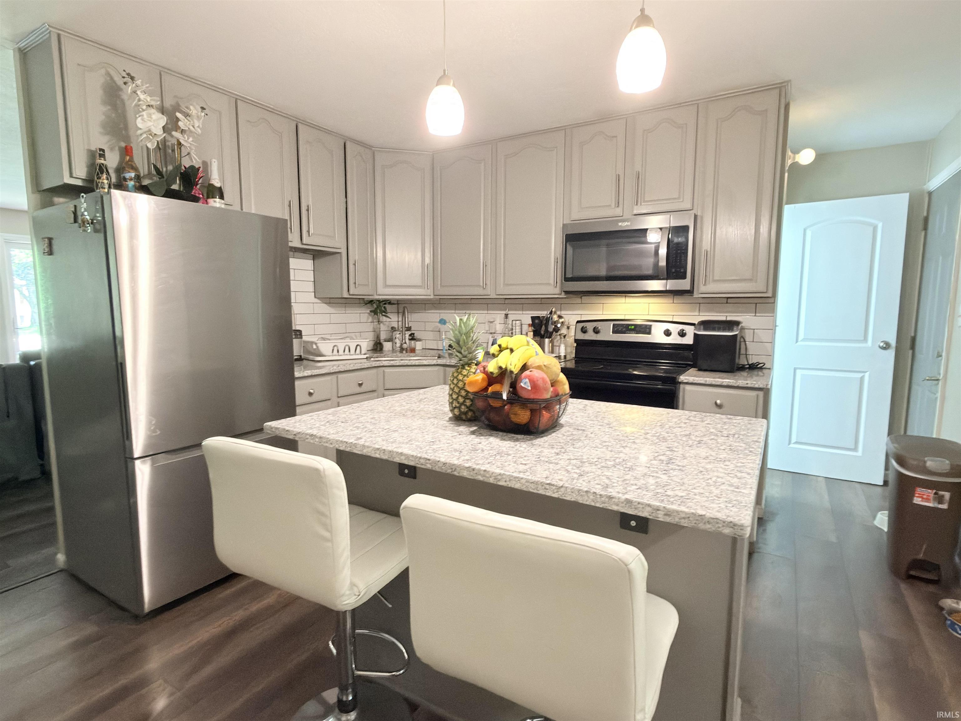Kitchen featuring light gray cabinetry, a central island with a light-toned countertop, stainless steel appliances, a white subway tile backsplash, and wood-finish flooring