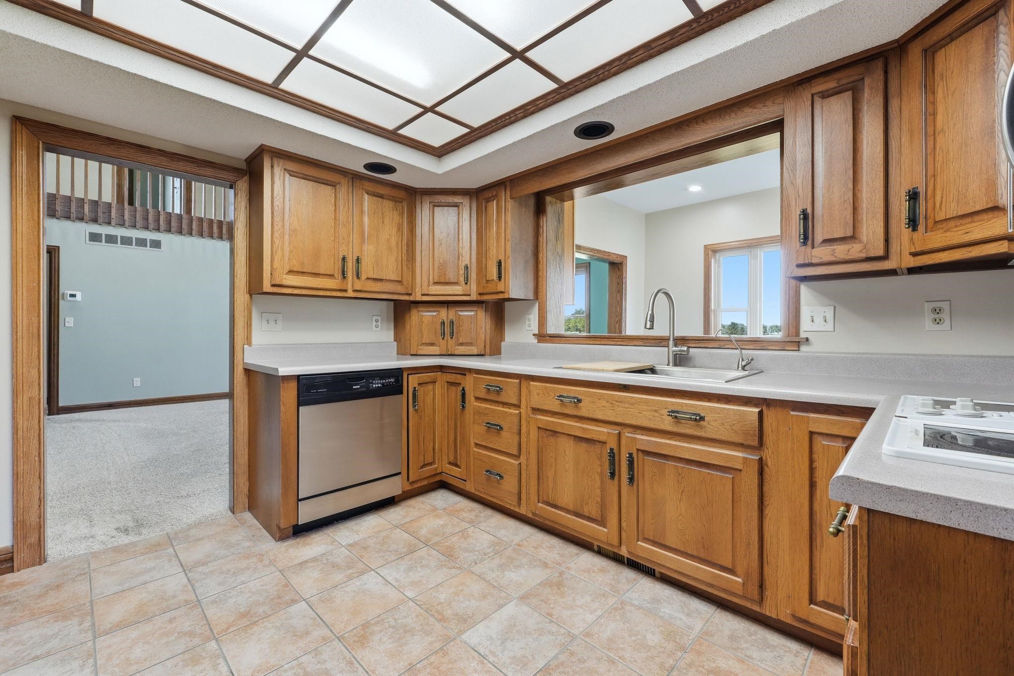 Kitchen featuring wood cabinetry, light-toned countertops, tile flooring, and a stainless steel dishwasher
