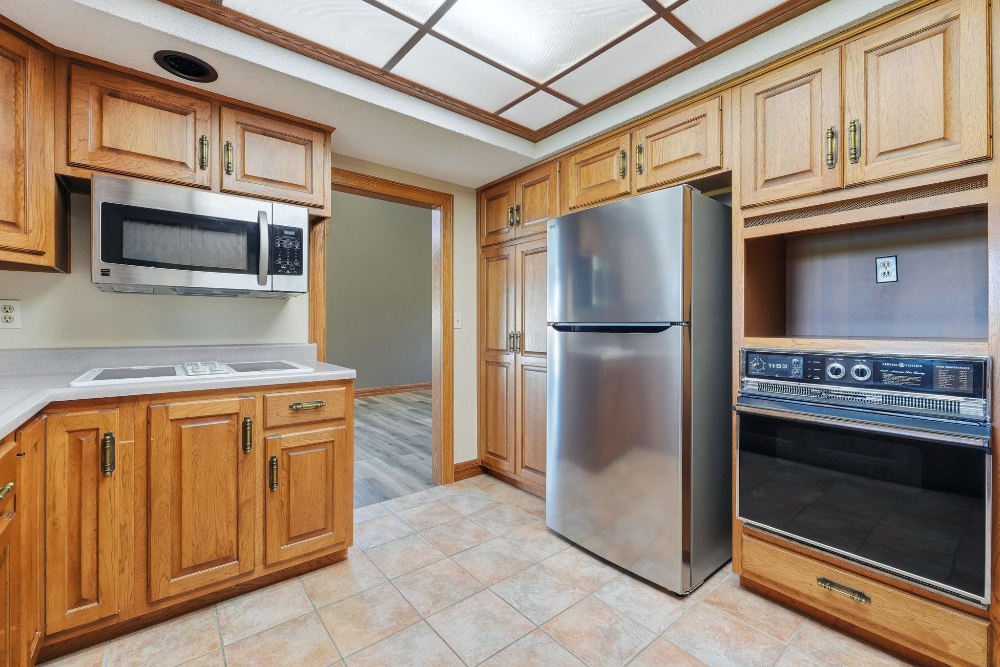Kitchen featuring light wood cabinetry with brass hardware, a built-in stainless steel microwave, a built-in wall oven, a stainless steel refrigerator, and tiled flooring