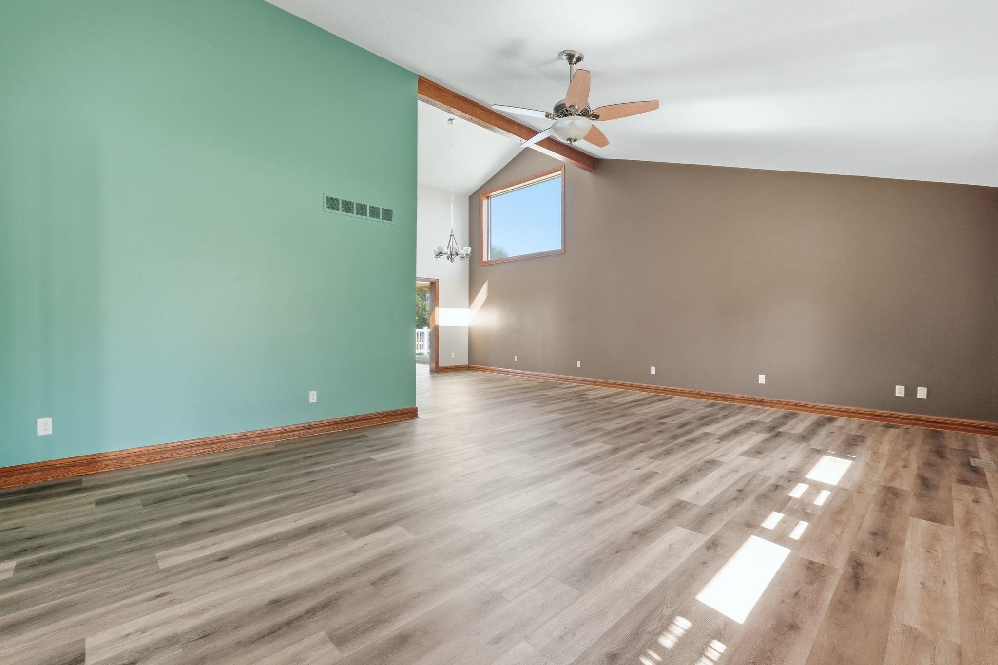 Spacious room featuring vaulted ceilings with exposed wood beams, a ceiling fan, and wood-finish flooring