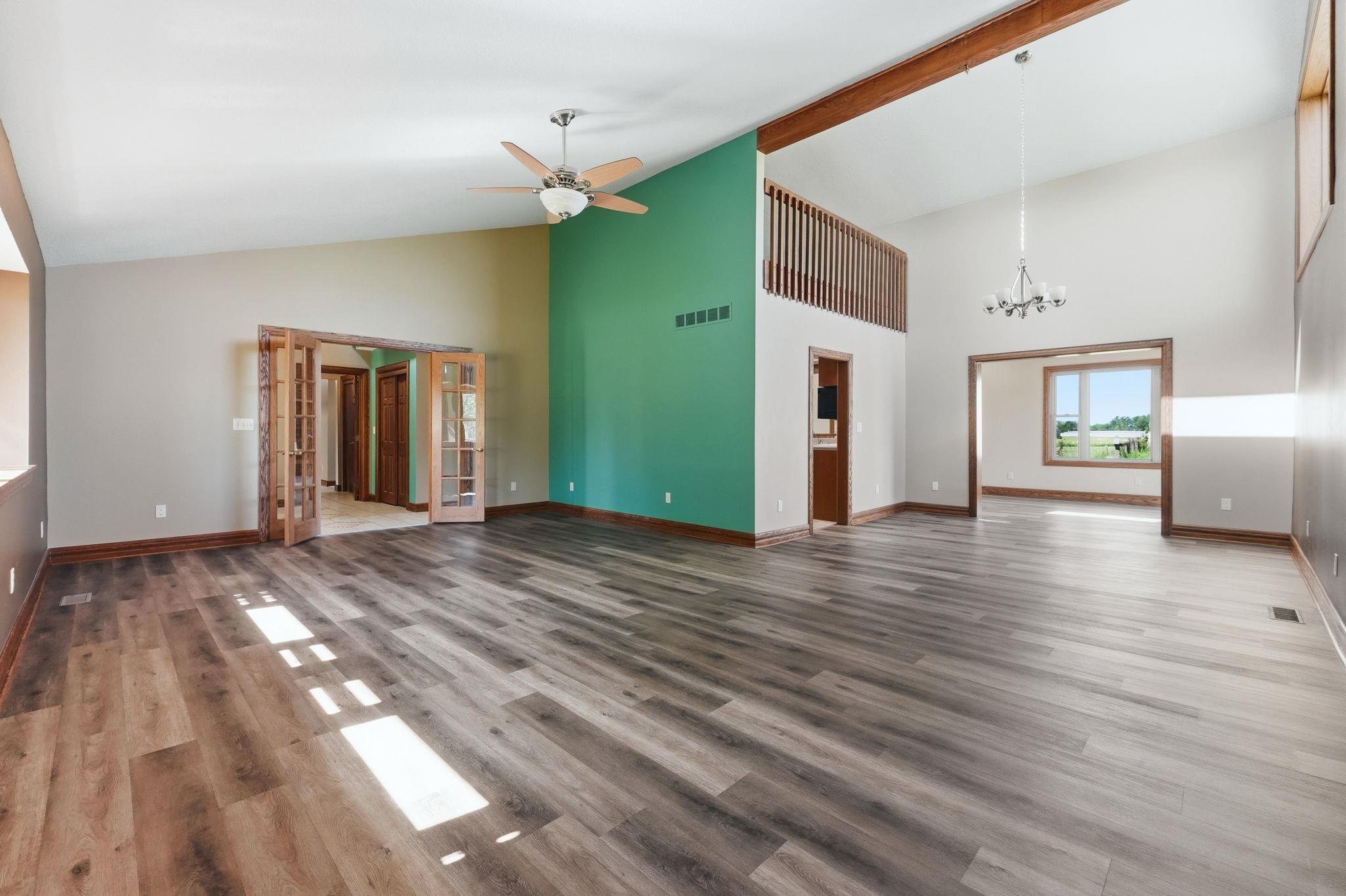 Expansive room featuring wood-finish flooring, vaulted ceilings, a prominent exposed wood beam, and a second-story balcony overlook