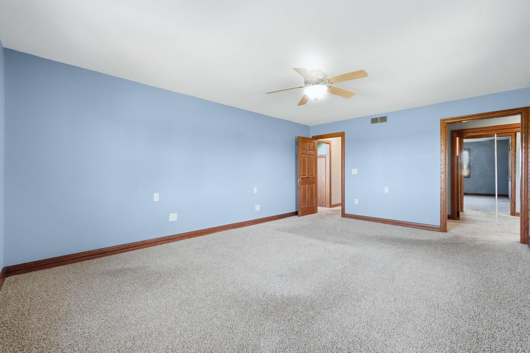 Spacious room featuring light blue walls, wood-finish trim, and plush carpet flooring