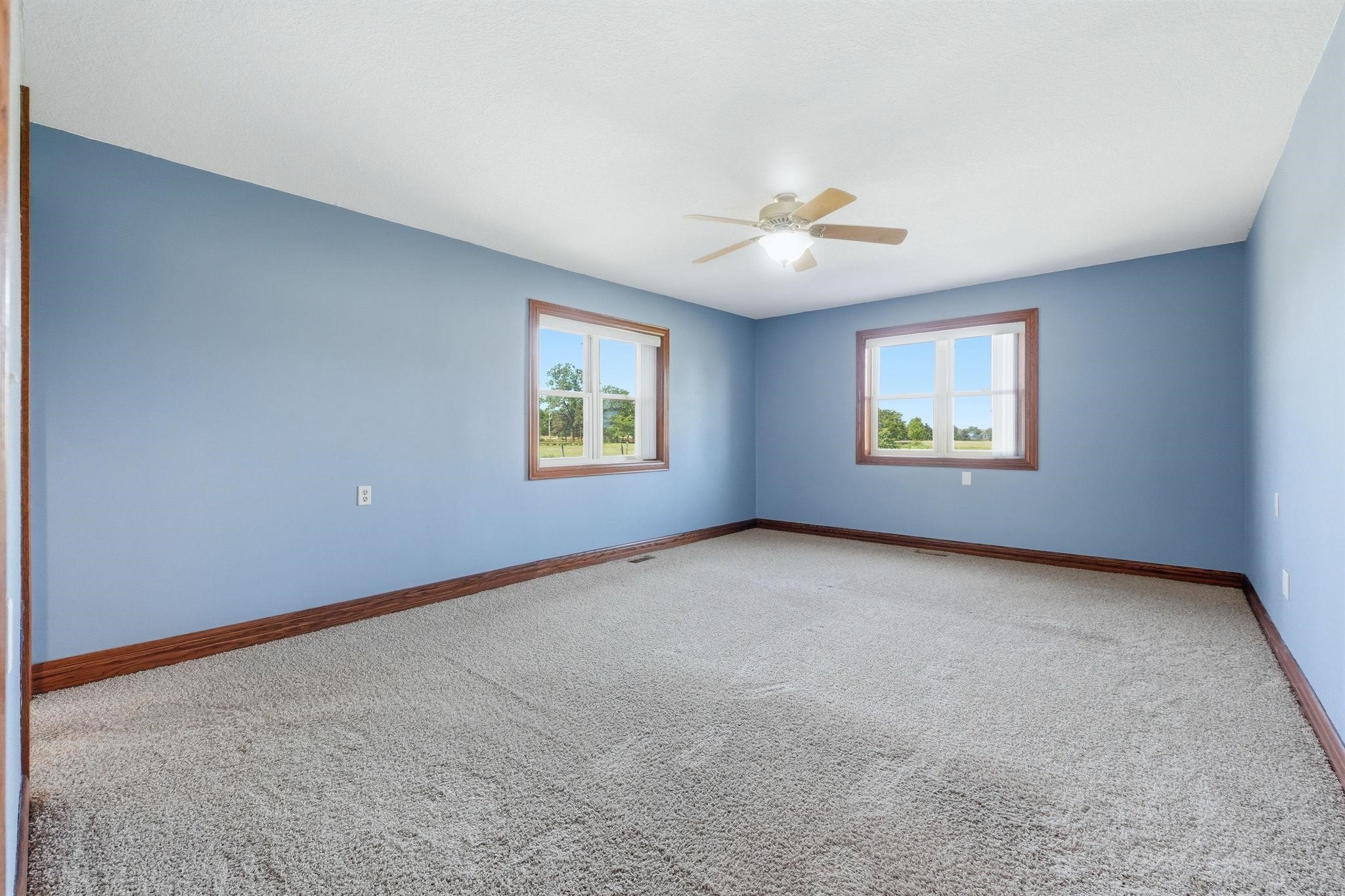 Spacious room featuring light blue walls, wood-finish trim, and light-colored carpeting