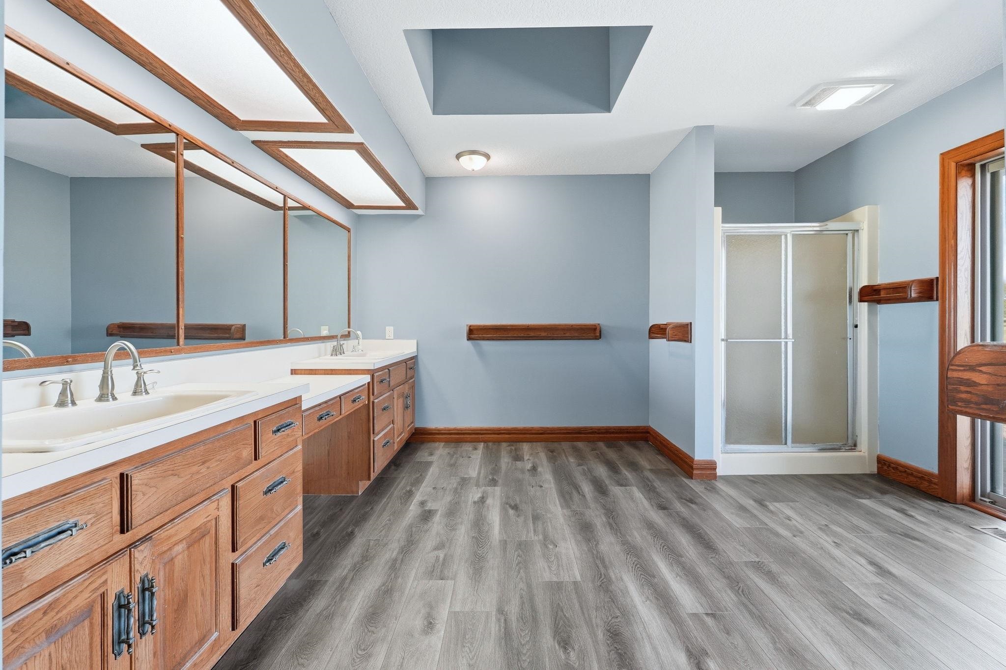 Spacious bathroom featuring a dual vanity with wood cabinetry, light countertops, and multiple mirrors