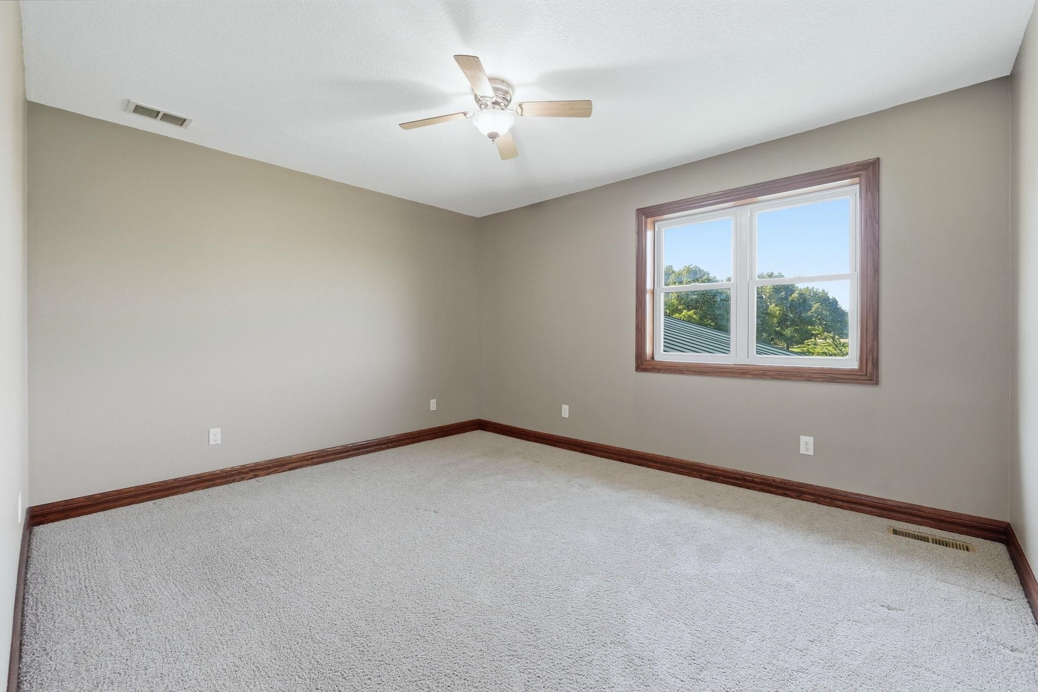 Carpeted room featuring a single window with wood-finish trim, light gray walls, a ceiling fan, and dark wood-finish baseboards