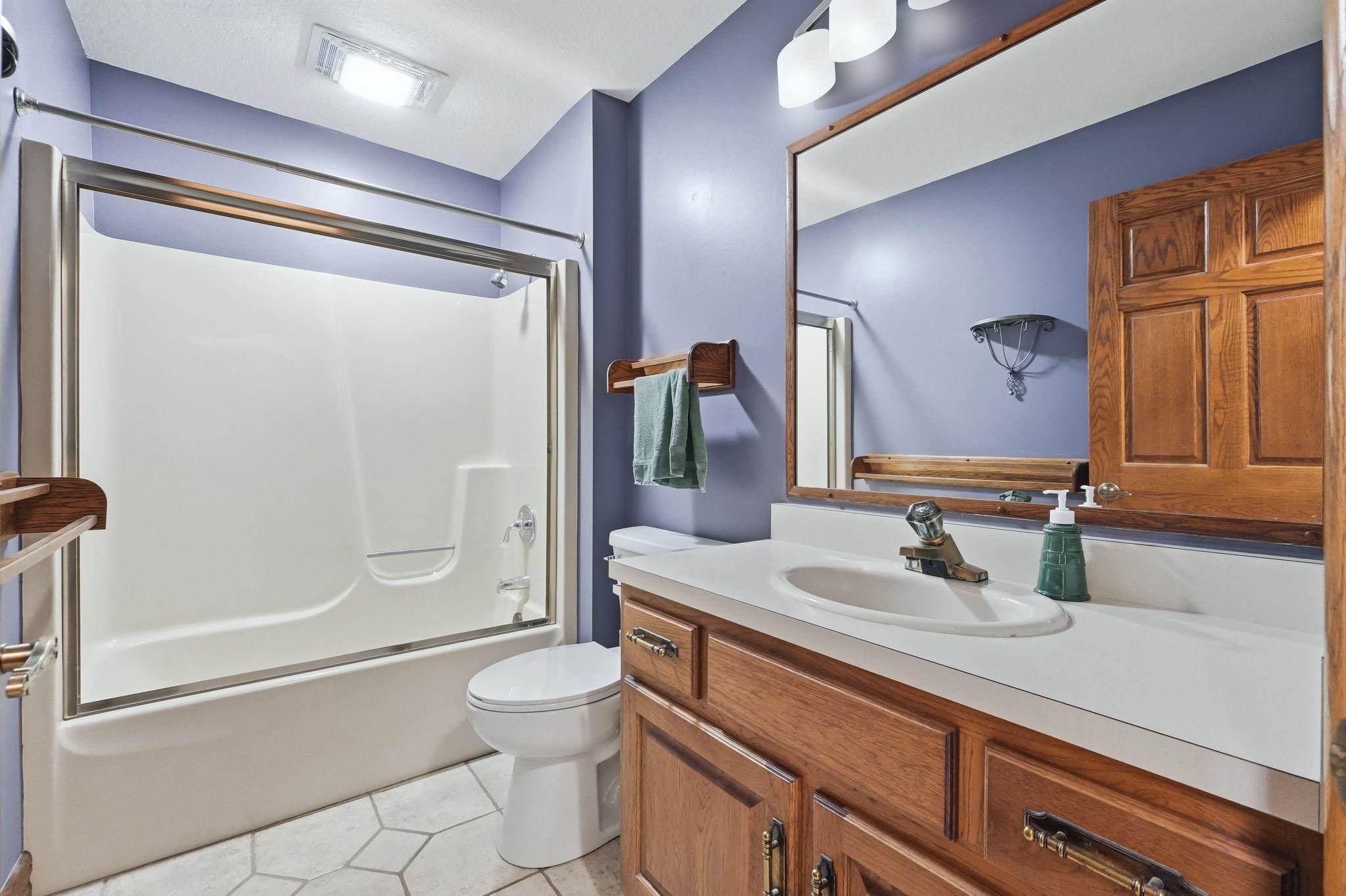Bathroom featuring a combination bathtub and shower with sliding glass doors, a single vanity with wood-finish cabinetry, an integrated sink, a large wall-mounted mirror, and hexagonal floor tiling