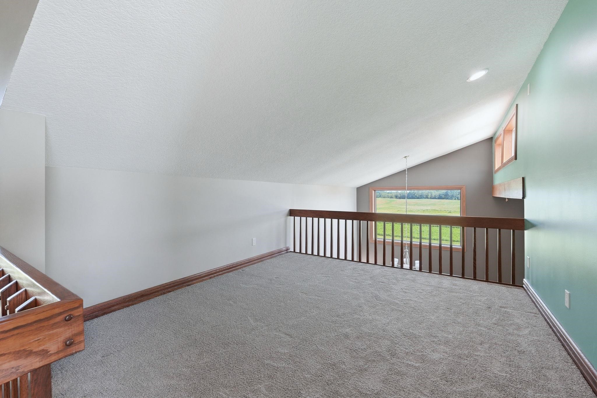 Carpeted loft area featuring a vaulted ceiling and a wood-finish railing overlooking the lower level
