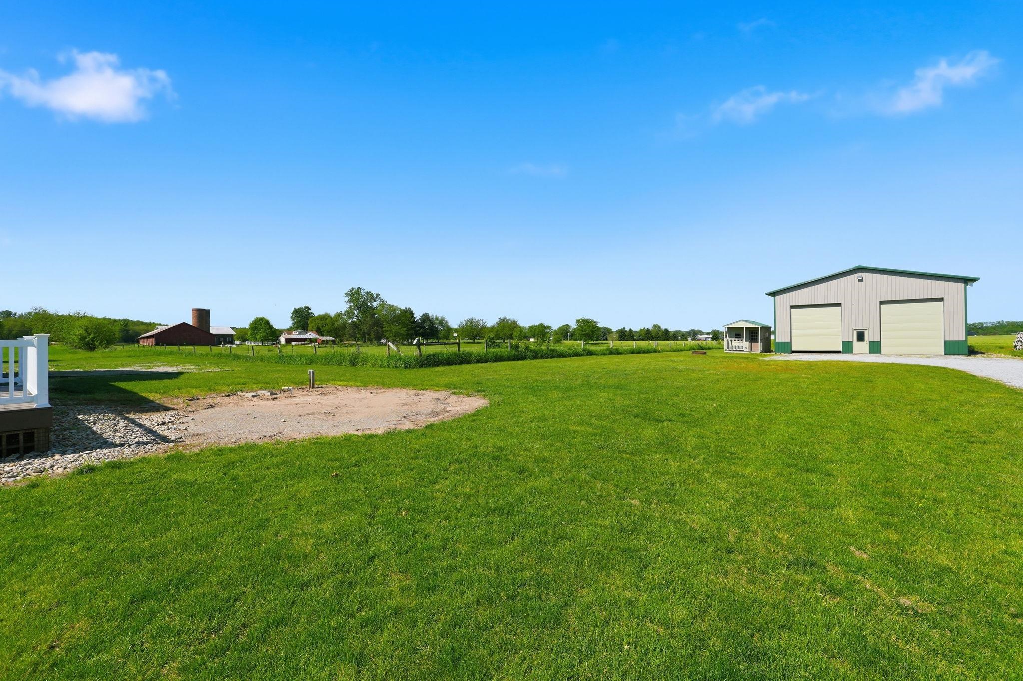Expansive green lawn with a large metal-sided outbuilding featuring two garage doors and an additional side entry