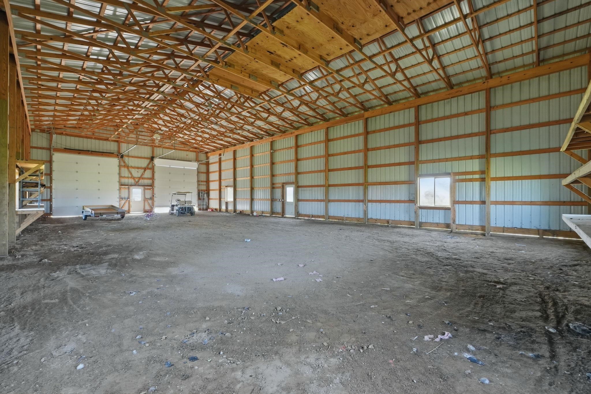 Spacious barn interior featuring exposed wood beam ceiling, corrugated metal walls, multiple entry doors, and a large roll-up door