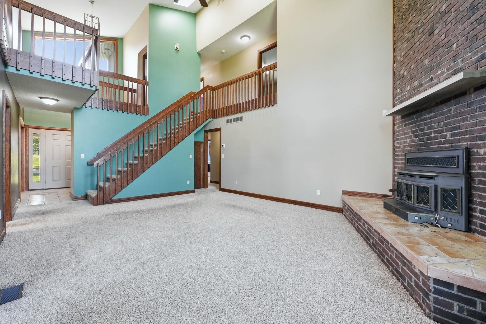 Two-story foyer with a wood staircase, carpeted living area, brick fireplace with tile hearth, and a windowed front door