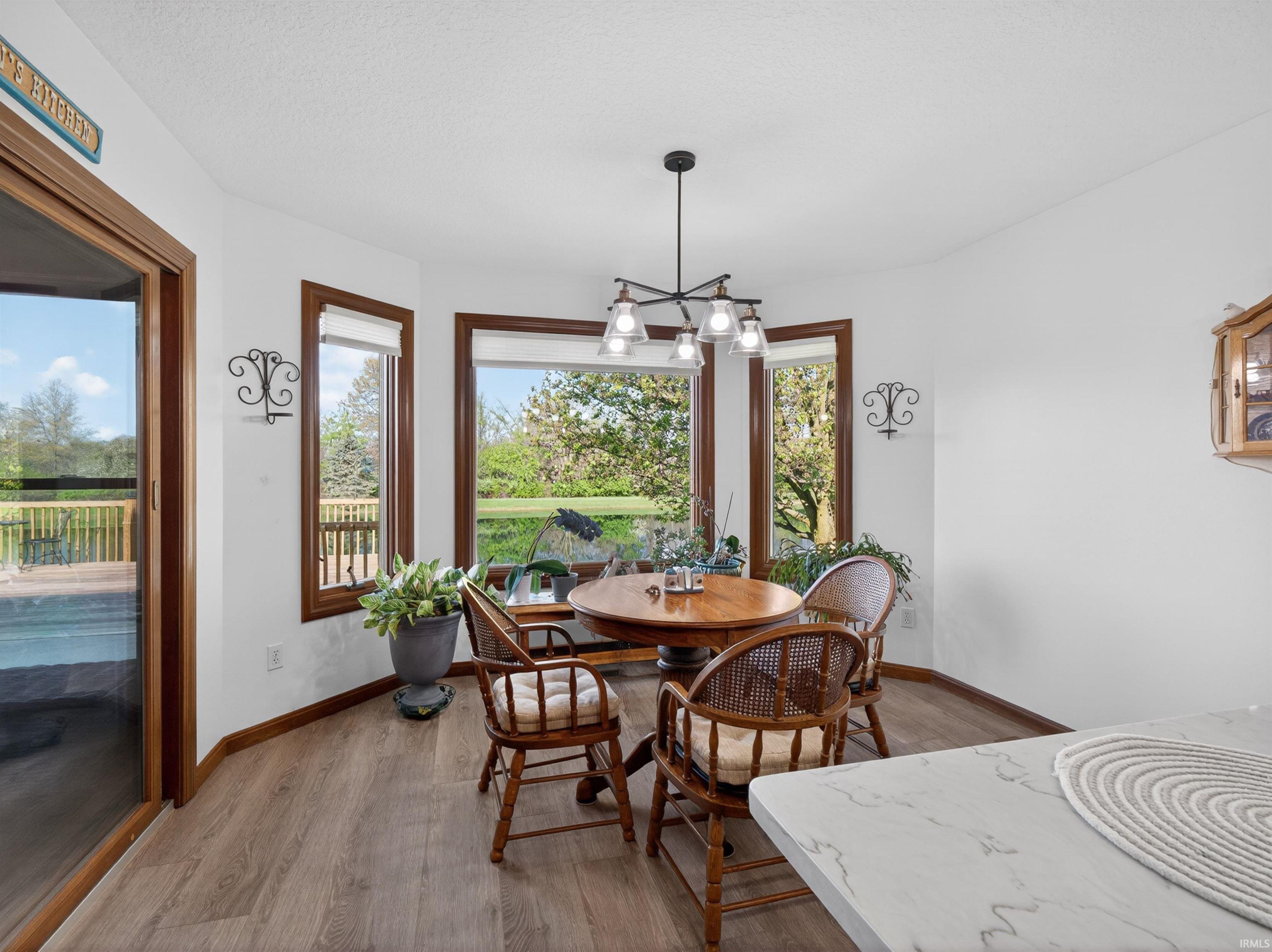 Bay window dining area featuring WATER VIEW, RESILIENT PREMIUM flooring, a modern chandelier, and a sliding glass door into SUNROOM. Light is wired for a ceiling fan.