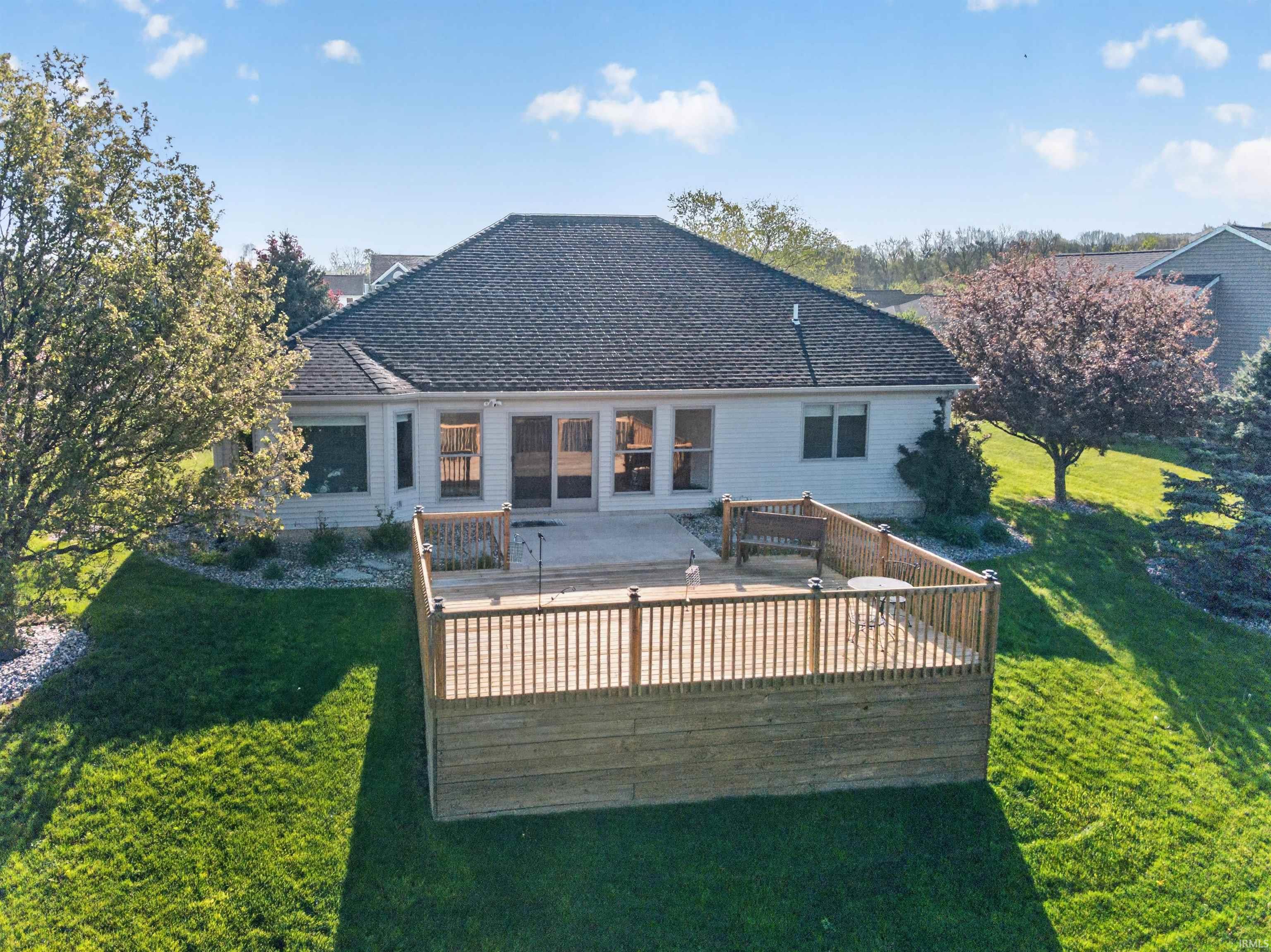 Rear exterior featuring a multi-level wooden deck with railings, a concrete patio, white siding, and a dark shingle roof