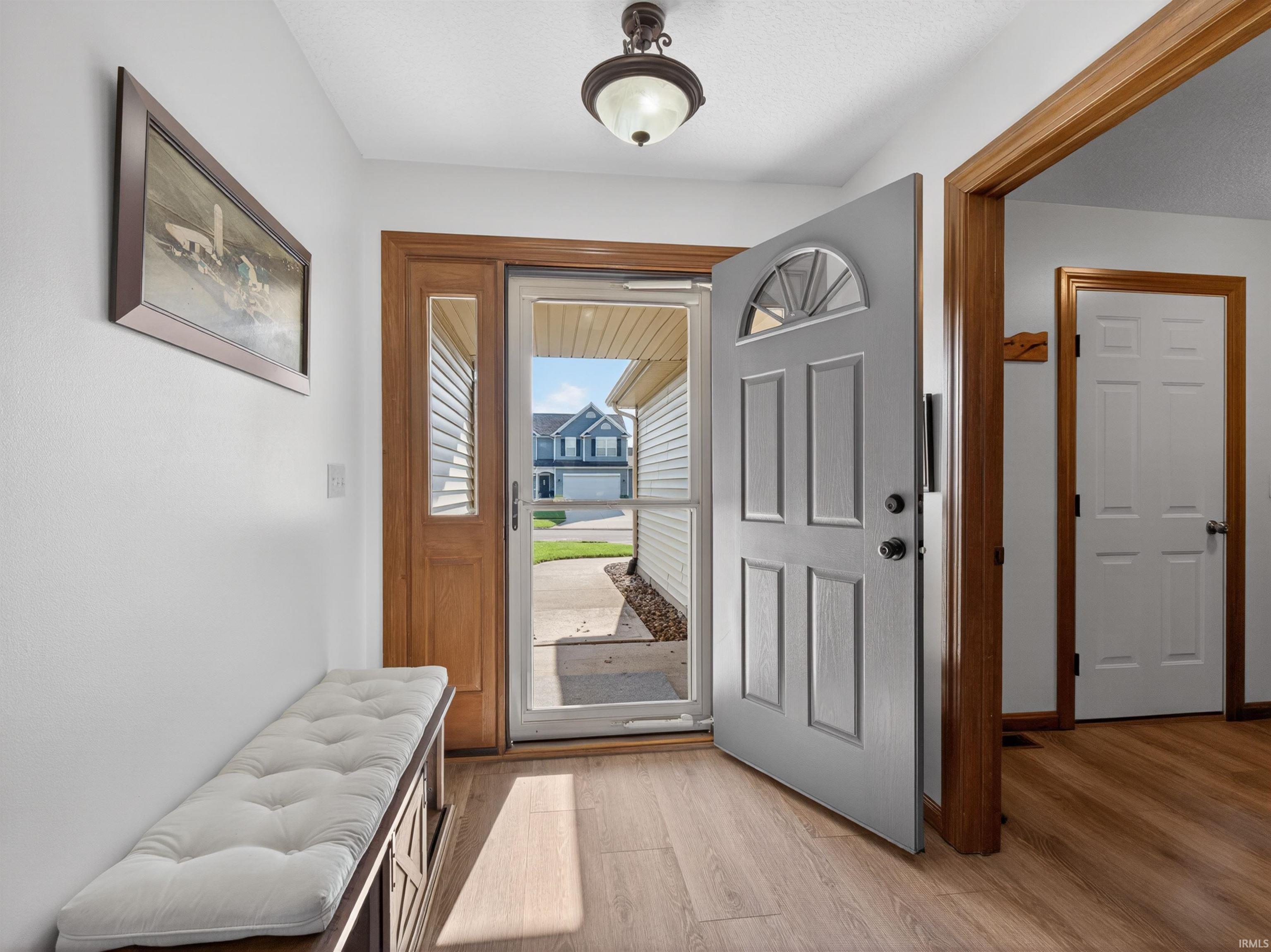 Welcoming entryway featuring premium resilient plank flooring, full glass storm door with screen inside, with an arched window, and a wood-framed sidelight.