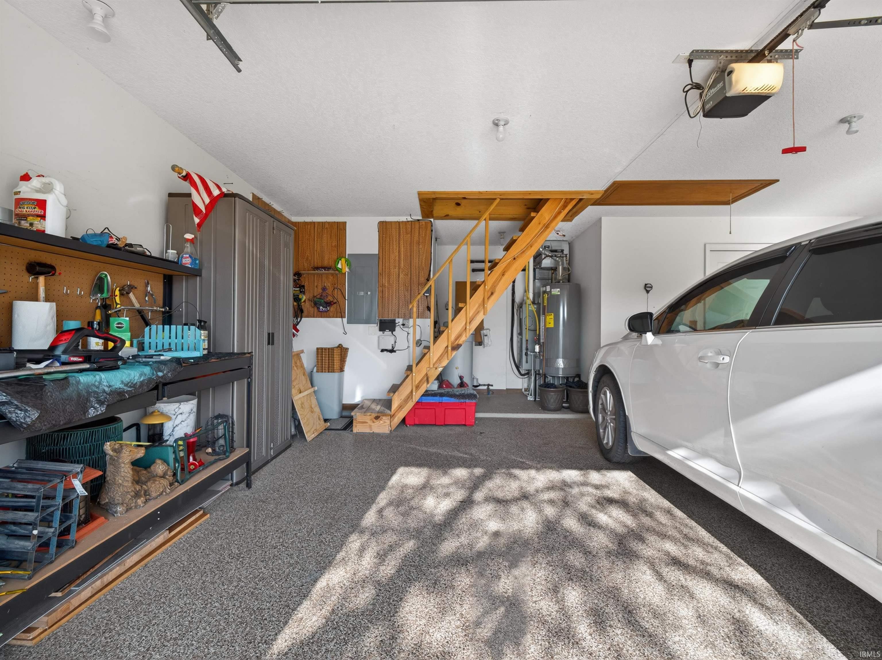 Spacious garage featuring epoxy flooring, PEG BOARD, ATTIC storage, and attic access via a wooden staircase.