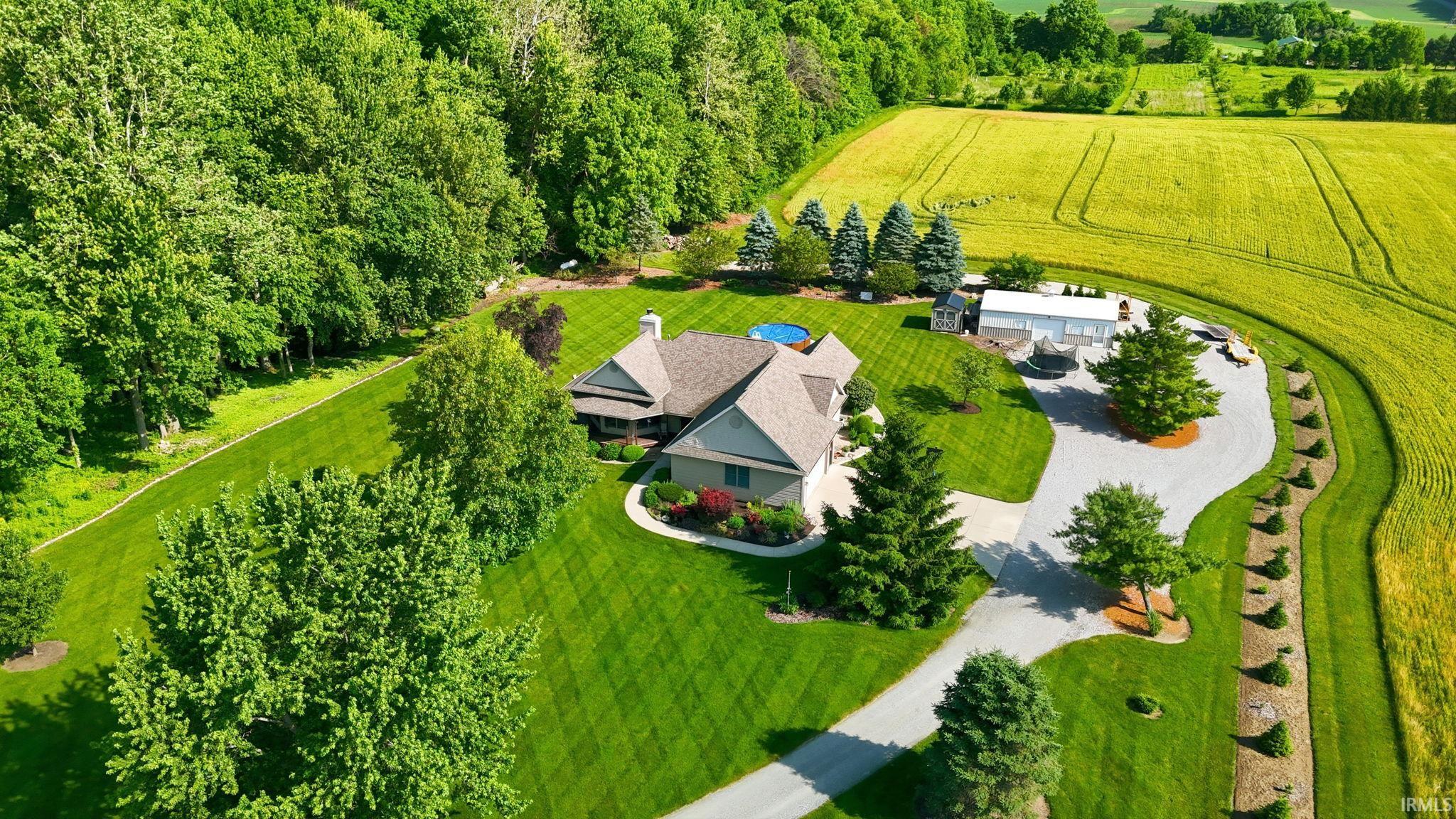 Spacious property featuring a large residence with a multi-gabled roofline, an expansive circular driveway, a detached outbuilding, and mature trees encompassing the grounds