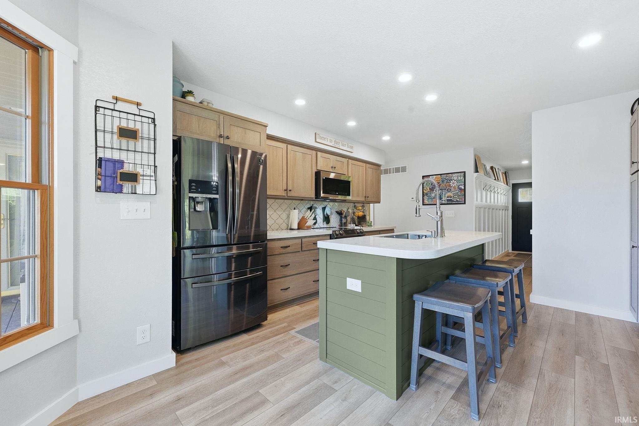 Kitchen featuring wood-finish flooring, a two-tone cabinetry scheme, and a kitchen island with a built-in sink and white countertop