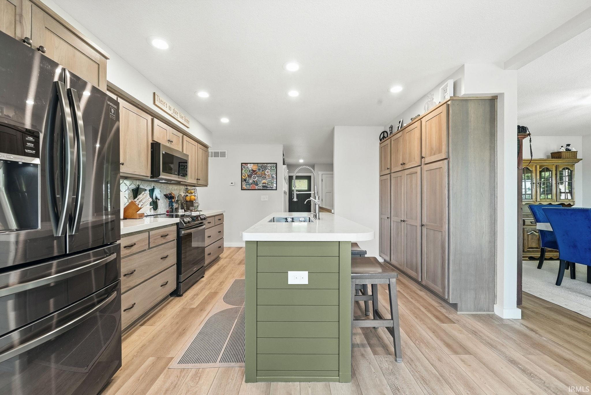Modern kitchen featuring a central island with a solid surface countertop, stainless steel appliances, wood-finish flooring, recessed lighting, and extensive cabinetry