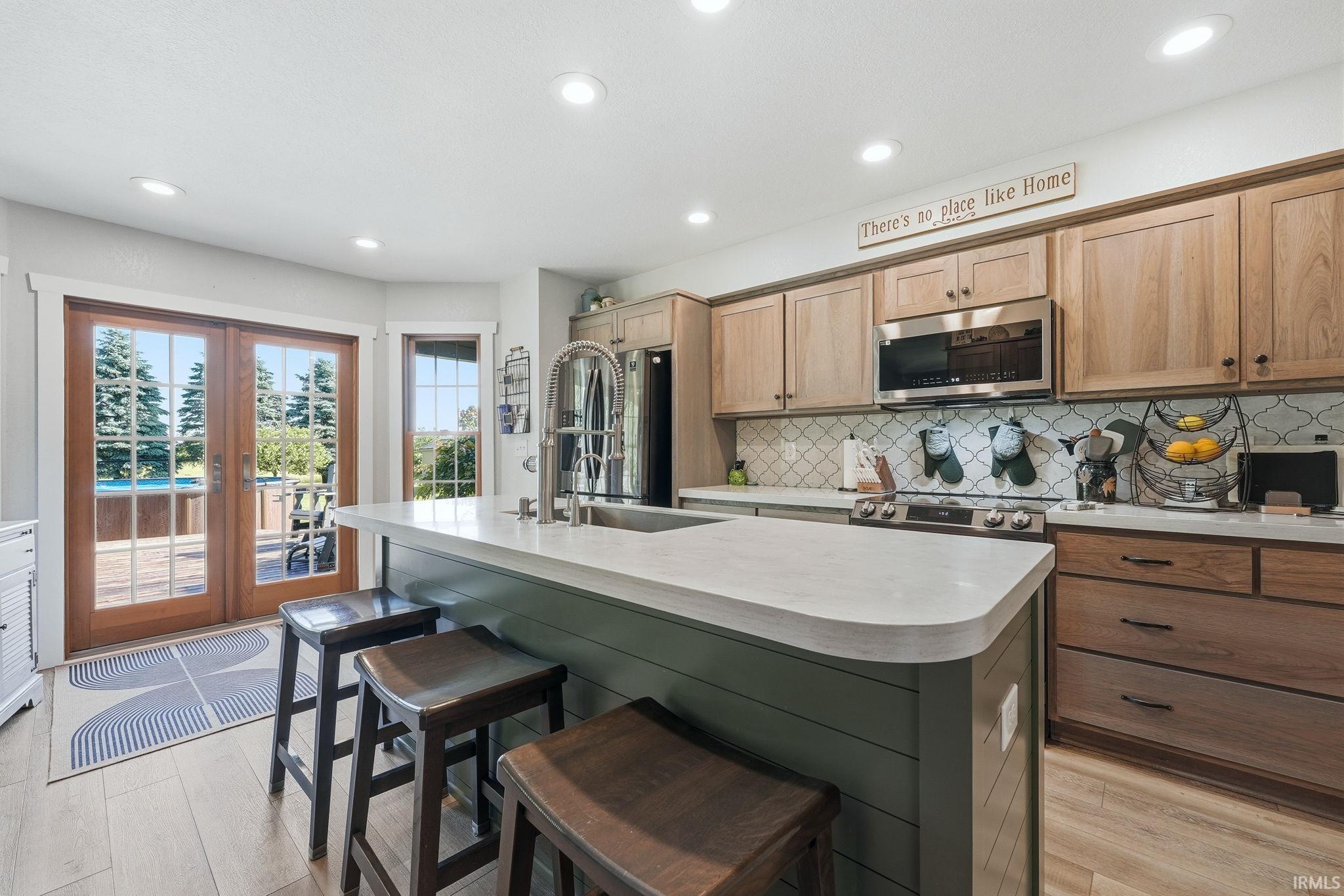 Kitchen featuring a central island with shiplap detailing and countertop seating, wood-finish cabinetry, stainless steel appliances, a decorative tile backsplash, and light wood-finish flooring