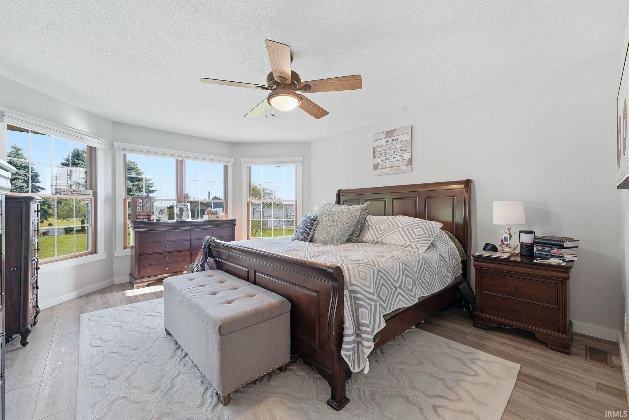 Bedroom featuring wood-finish flooring, a ceiling fan with integrated lighting, and multiple windows providing natural illumination