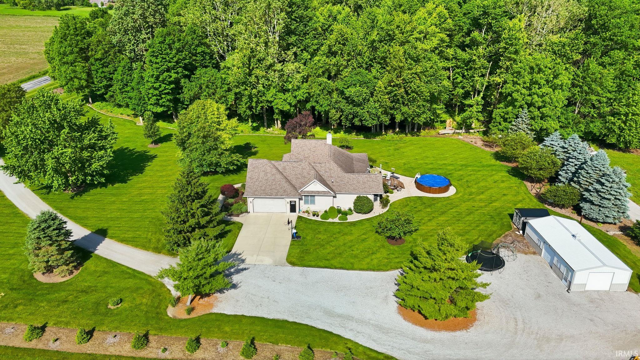 Expansive property featuring a single-story residence, detached outbuilding, gravel driveway, concrete driveway, and established landscaping