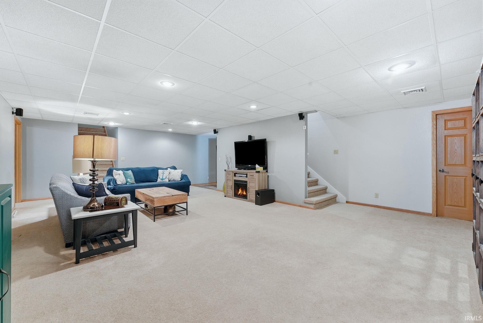 Spacious room featuring neutral carpet flooring, recessed lighting, drop ceiling, light gray wall paint, and a wood-finish door