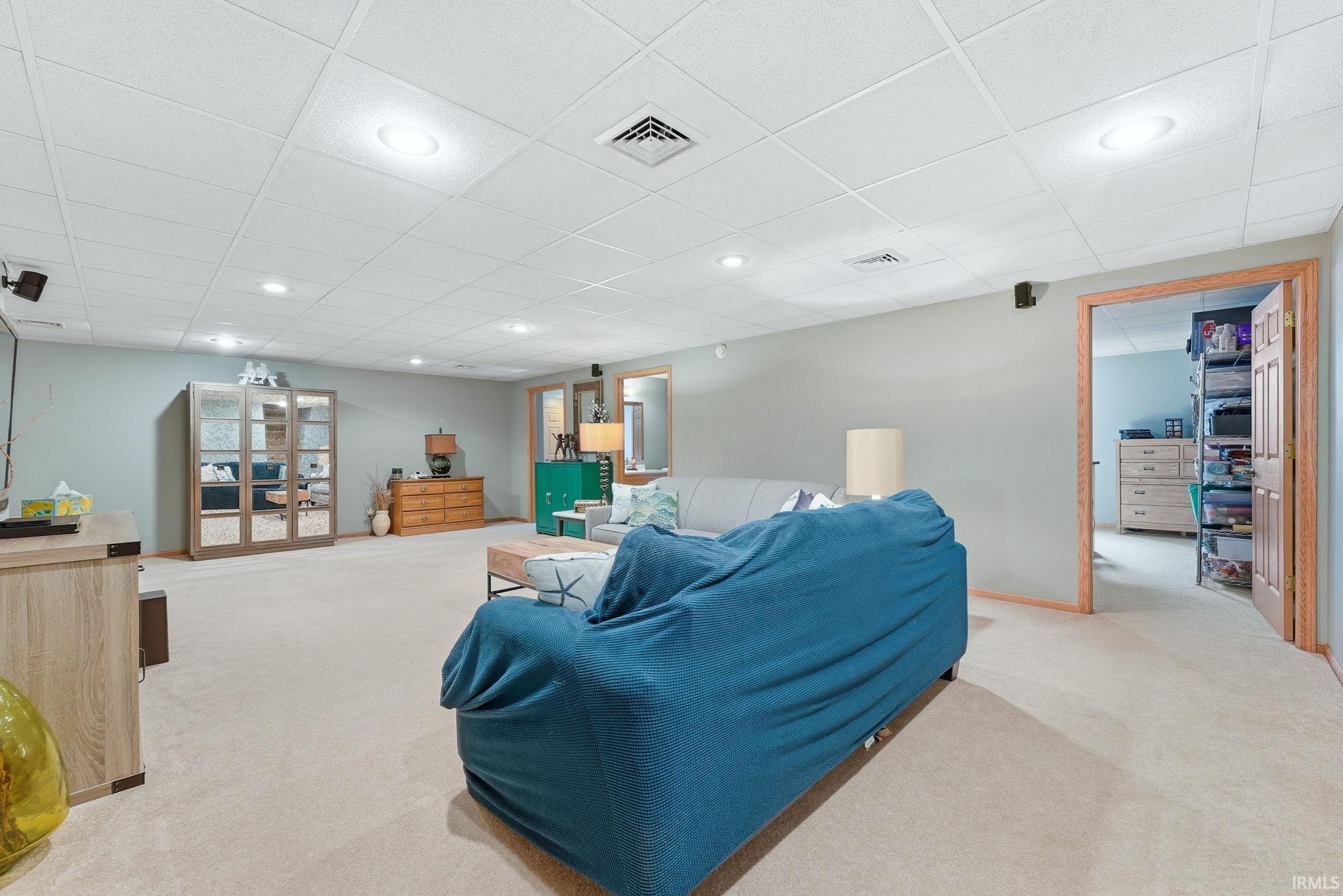 Spacious room featuring neutral carpeting, light blue walls, a white drop ceiling with recessed lighting, and a wood-framed doorway opening to another area