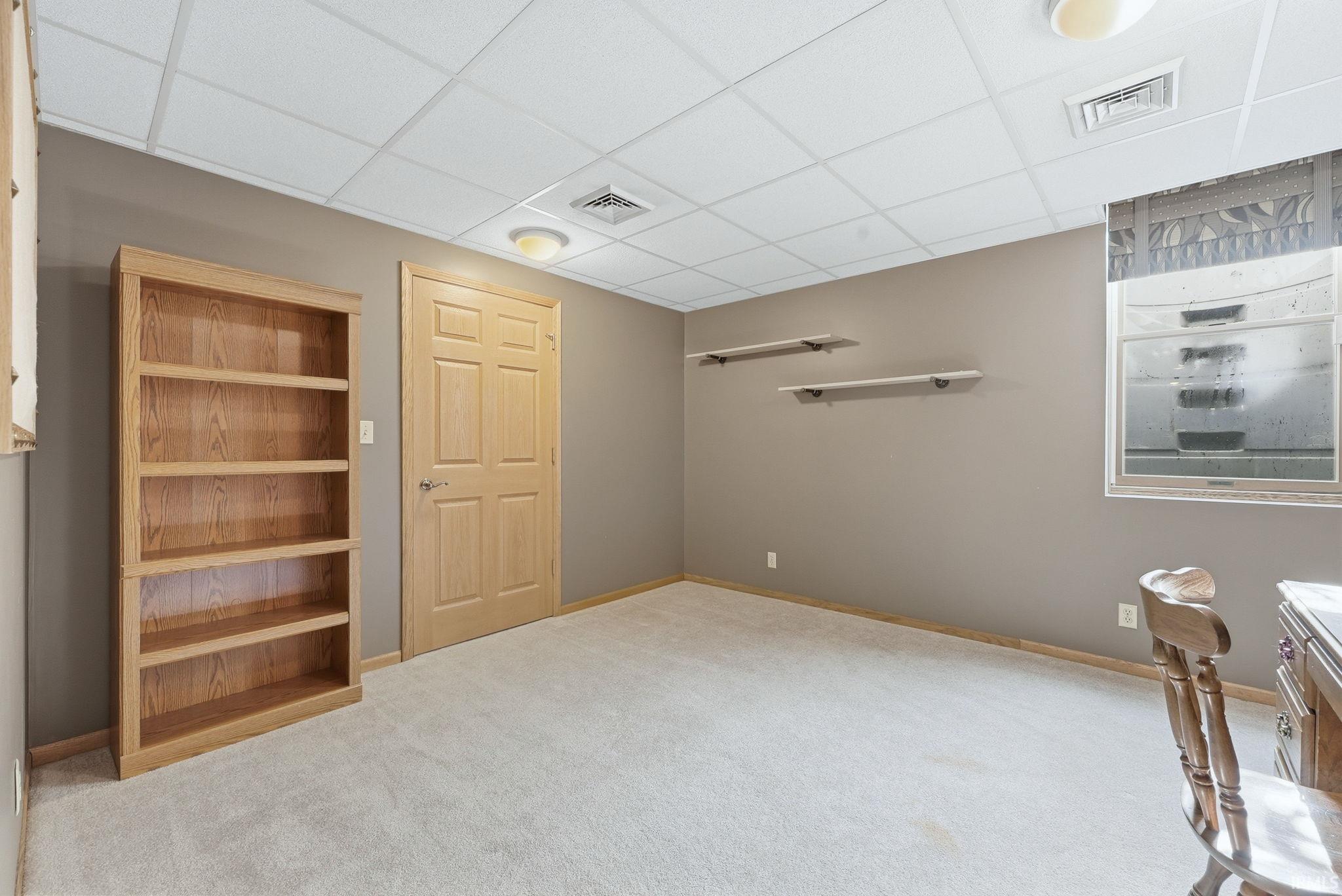 Carpeted room featuring a built-in wooden bookcase, a wood-finish door, and neutral painted walls
