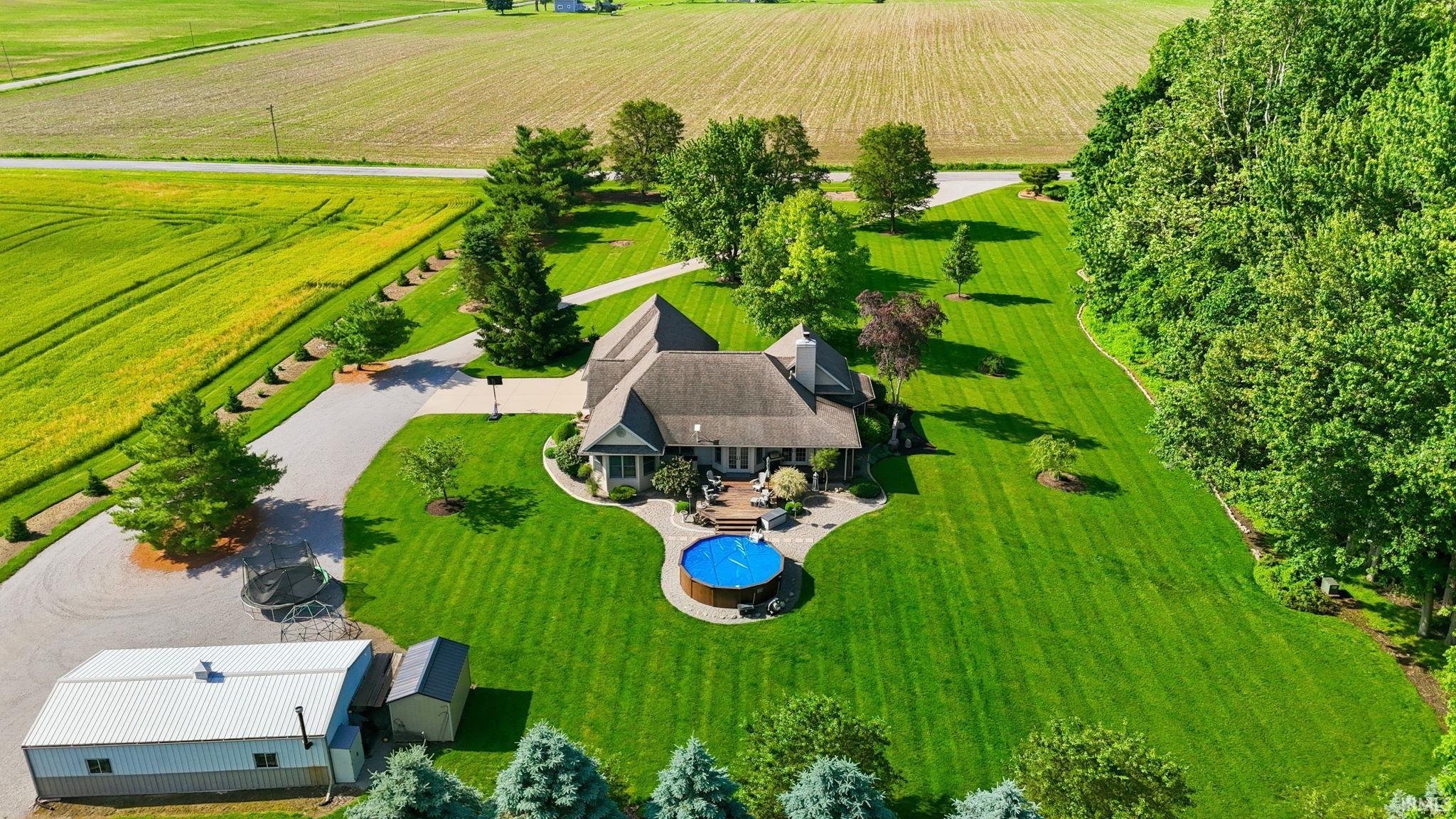 Spacious property featuring a large residence with an expansive green lawn, mature trees, and an above-ground pool