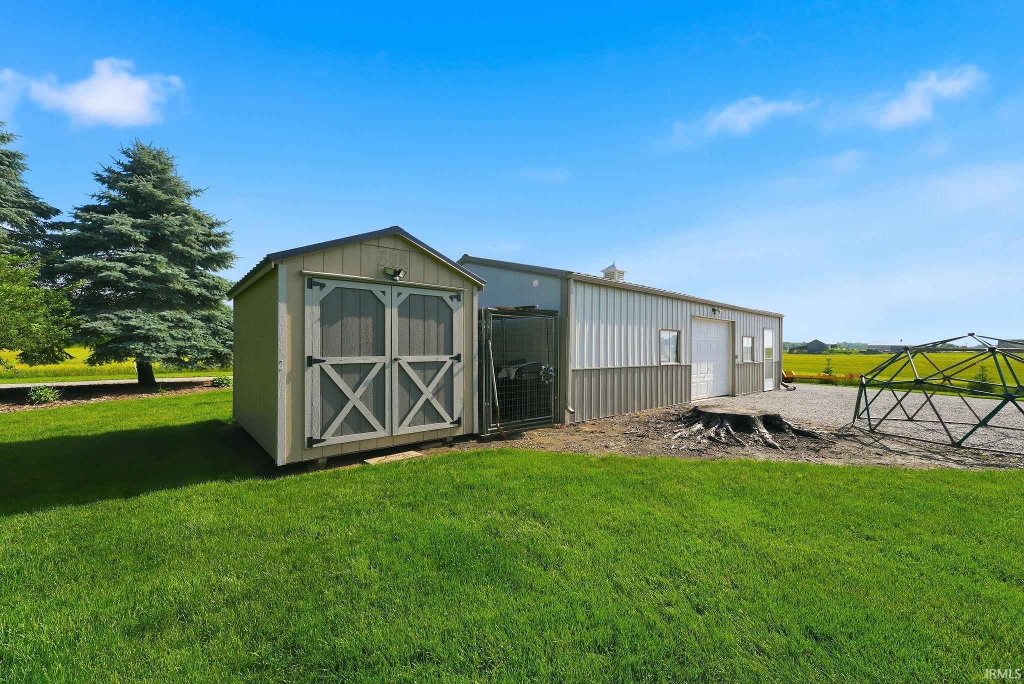 Expansive exterior featuring a light-colored utility shed with cross-brace doors, a large metal-sided outbuilding with a roll-up door, and a substantial green lawn